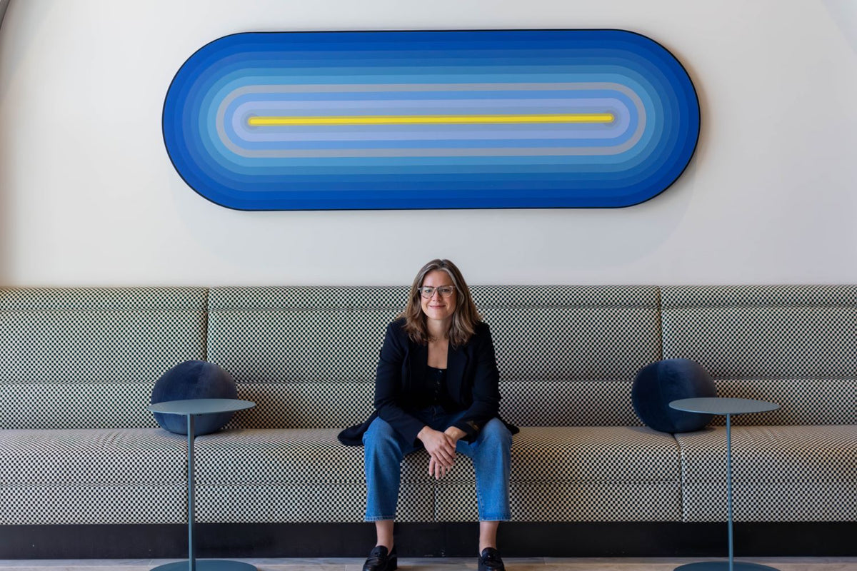 Designer Sheena Brittingham sitting on a bench looking forward with a large blue oval artwork behind her.