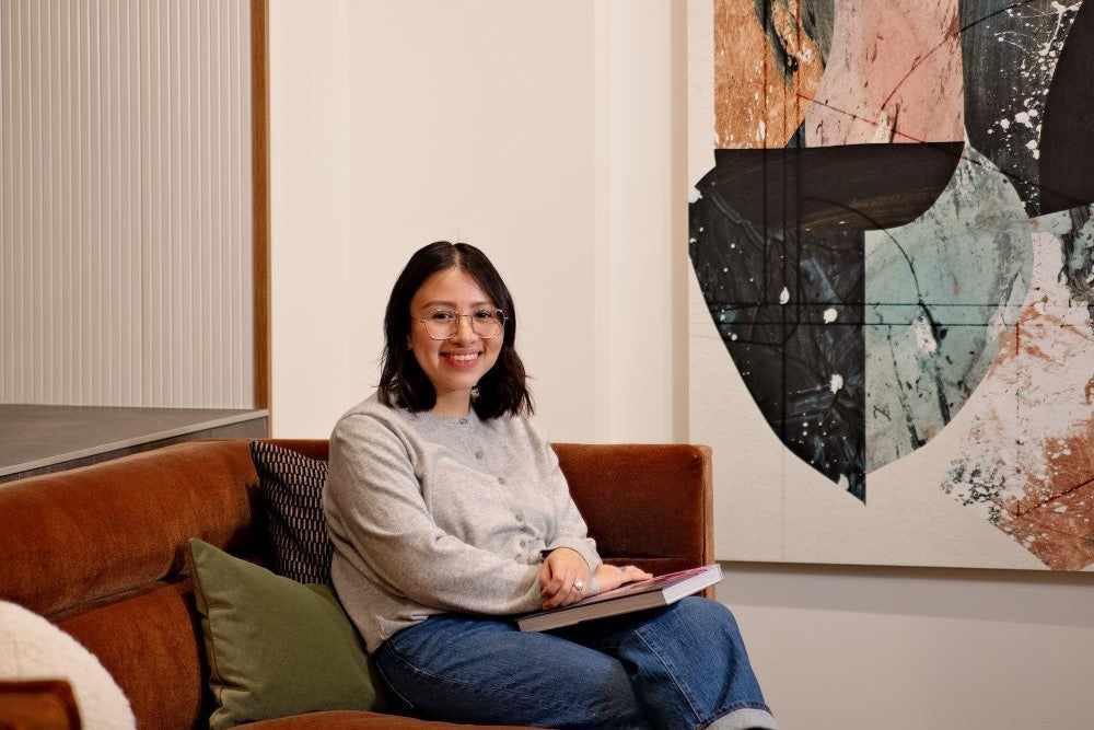 signer Jacqueline sitting on a sofa with a book on her lap, smiling at the camera