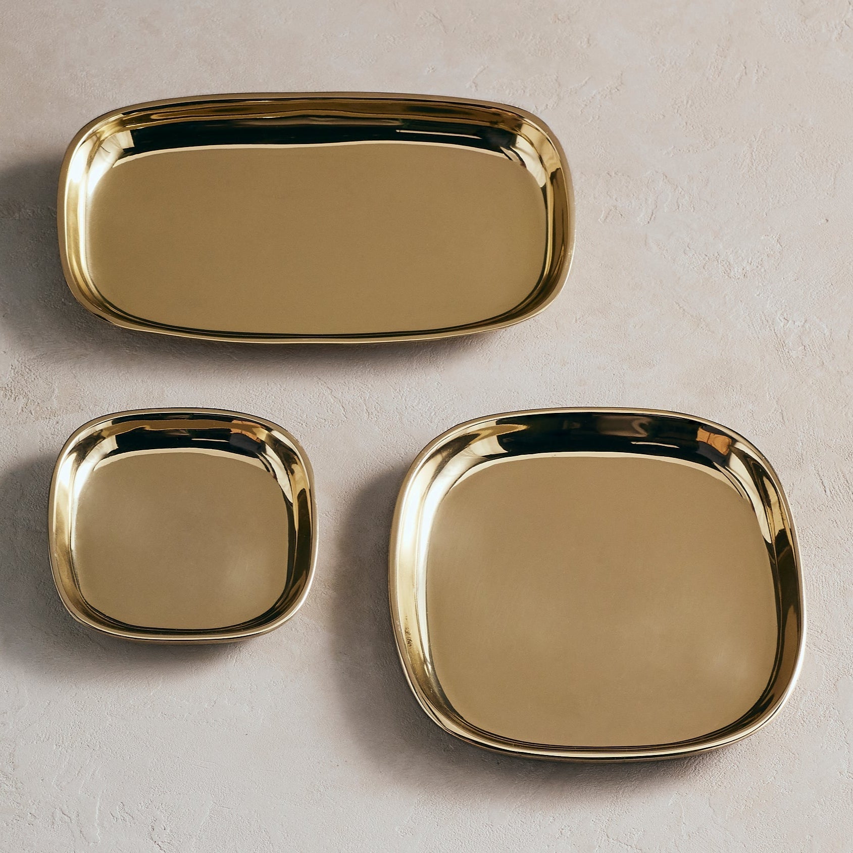 Three gold trays of different sizes on a light gray background