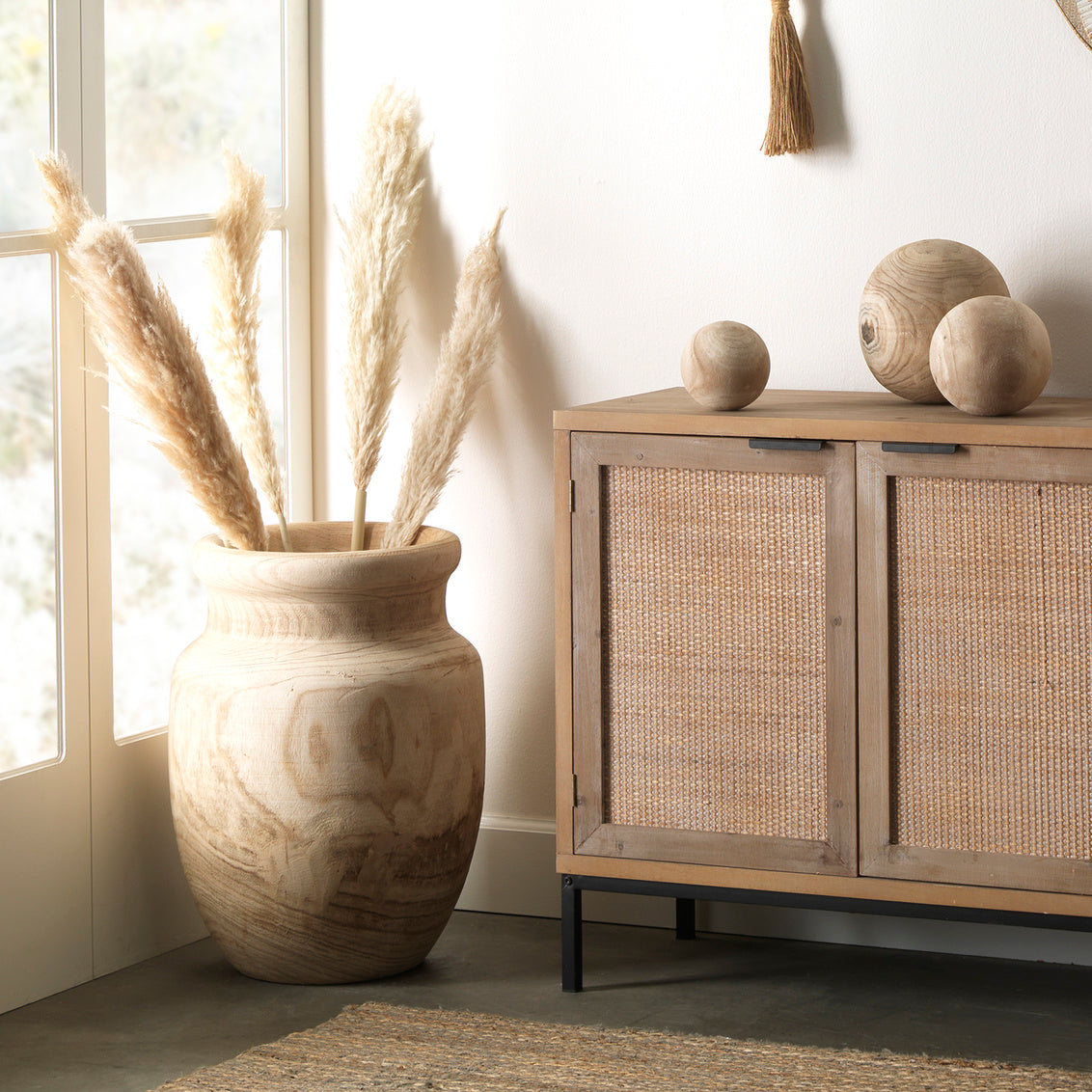 Decorative vase with dried plants next to a wooden cabinet with wicker doors.