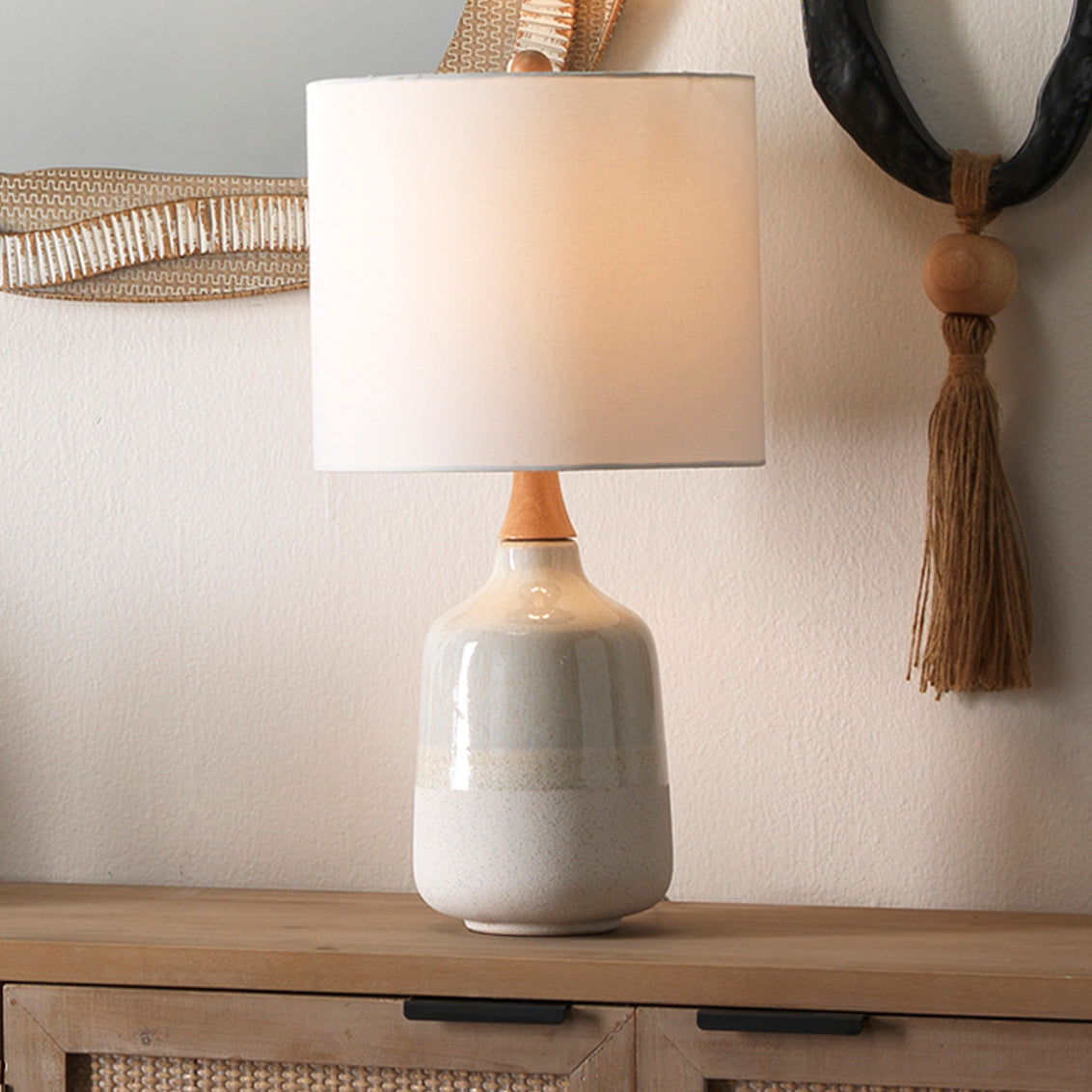 Table lamp with a white shade and ceramic base on a wooden surface.