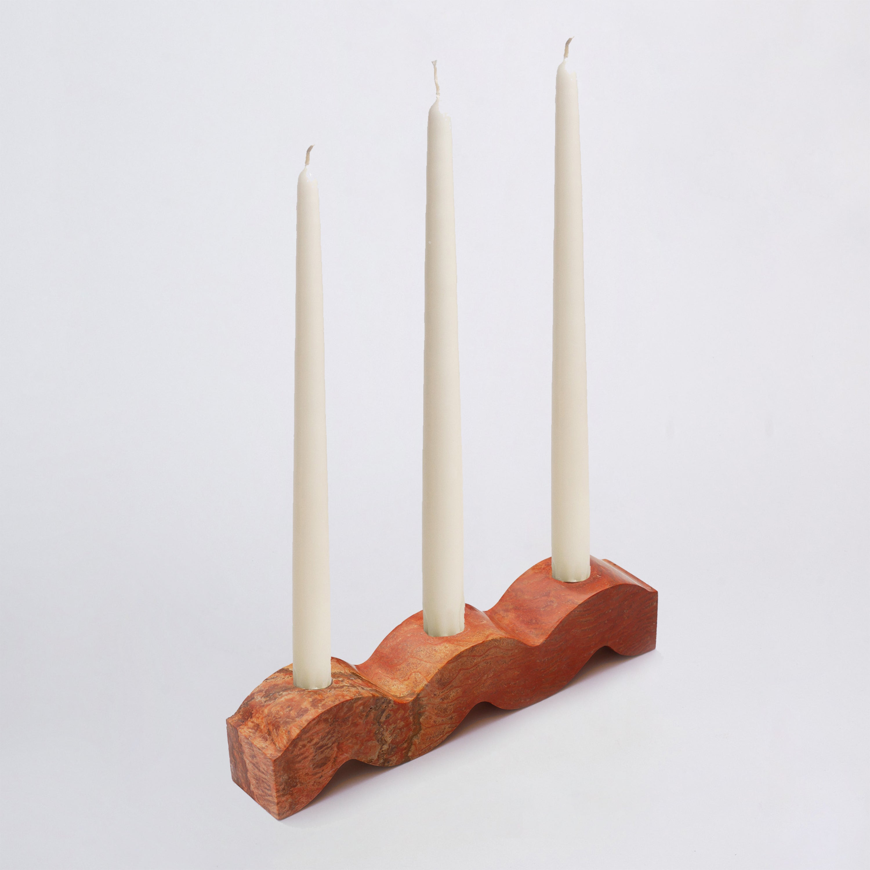 Stone candle holder with three white candles on a light gray background