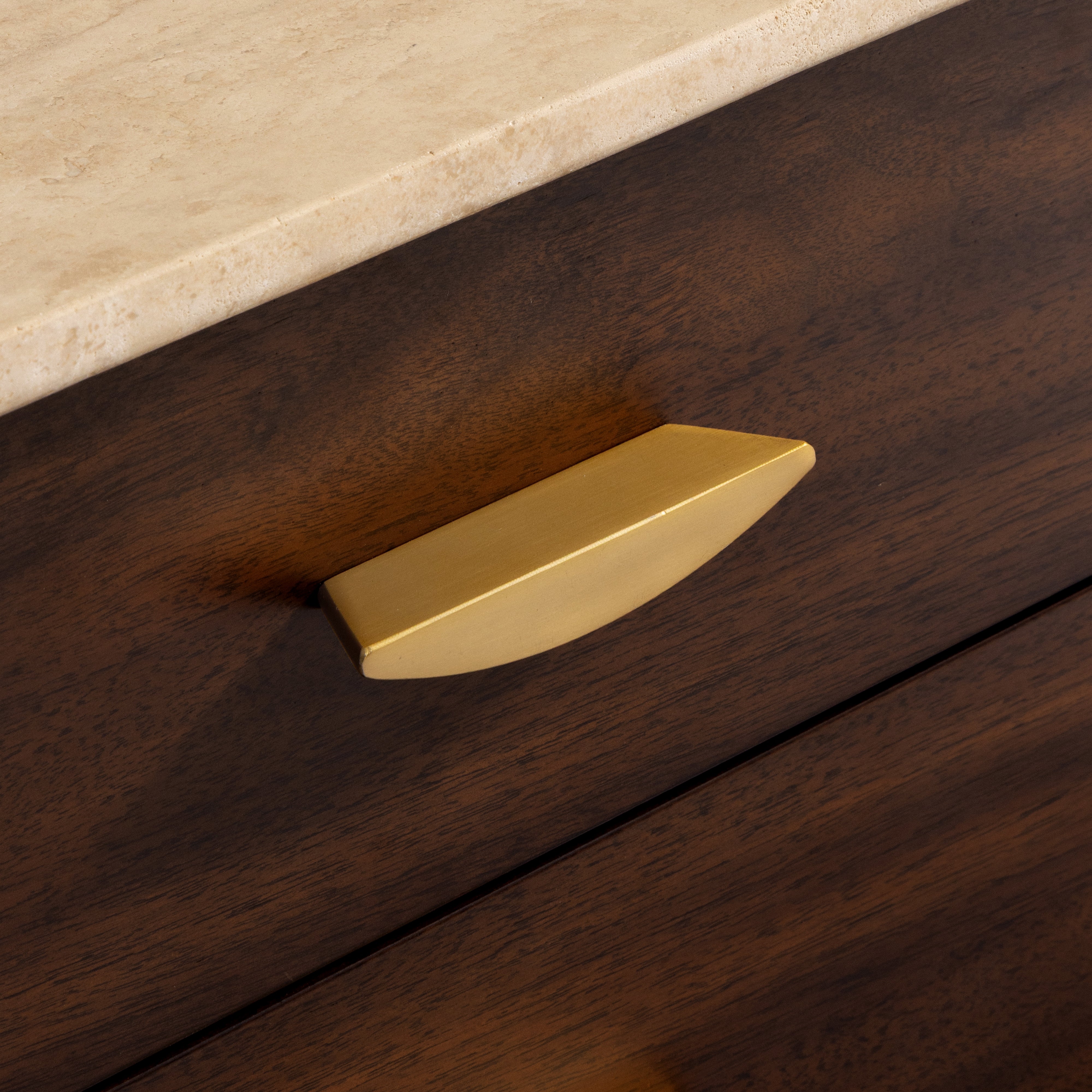 Gold cabinet handle on a wooden drawer with a beige countertop.