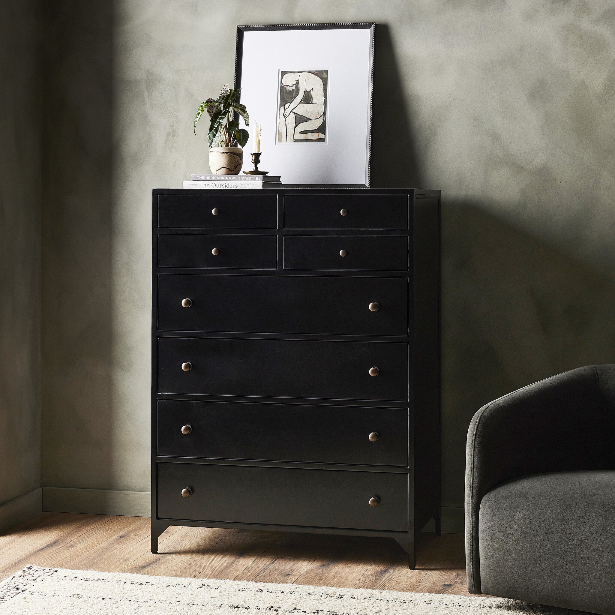 Black dresser with decorative items against a gray wall in a room with a gray armchair.