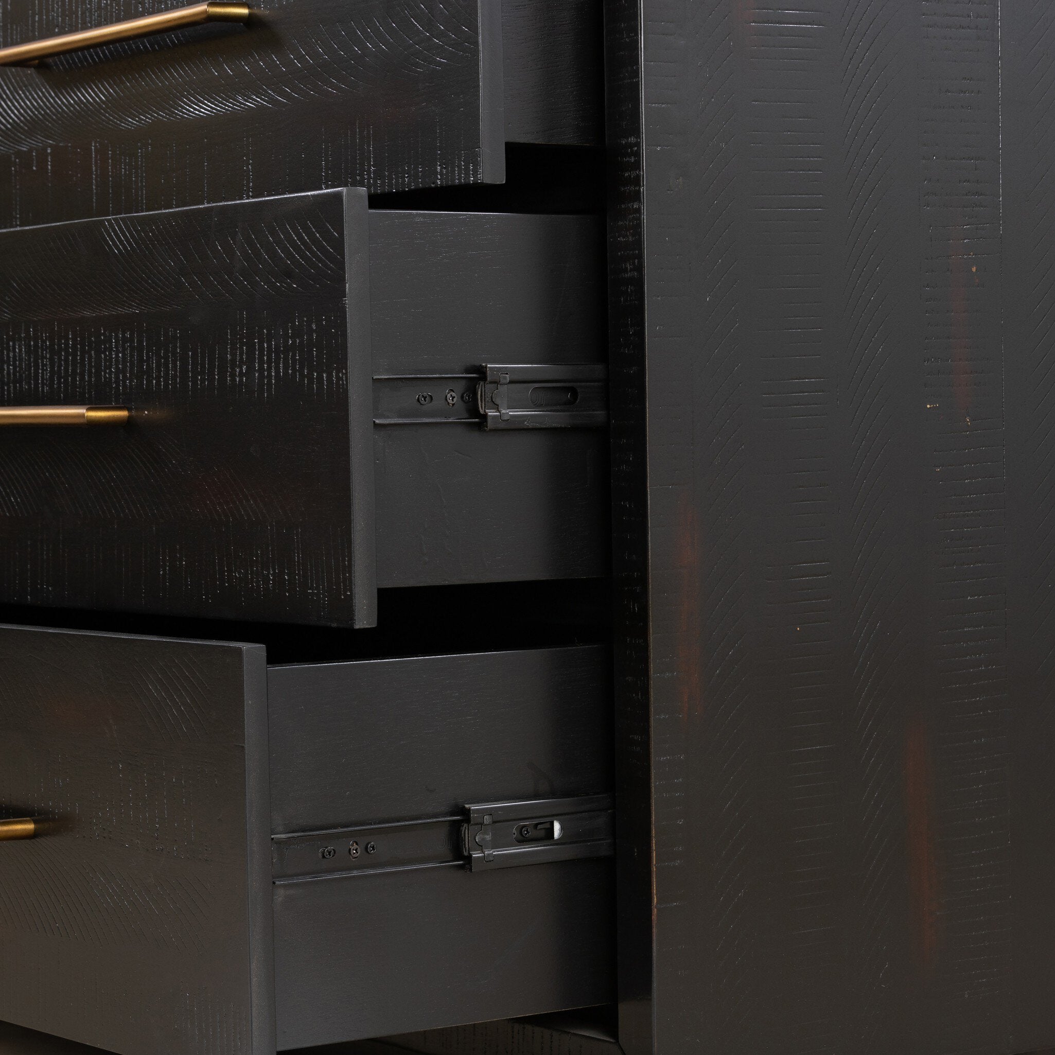Close-up of a dark wooden dresser with open drawers and gold handles.