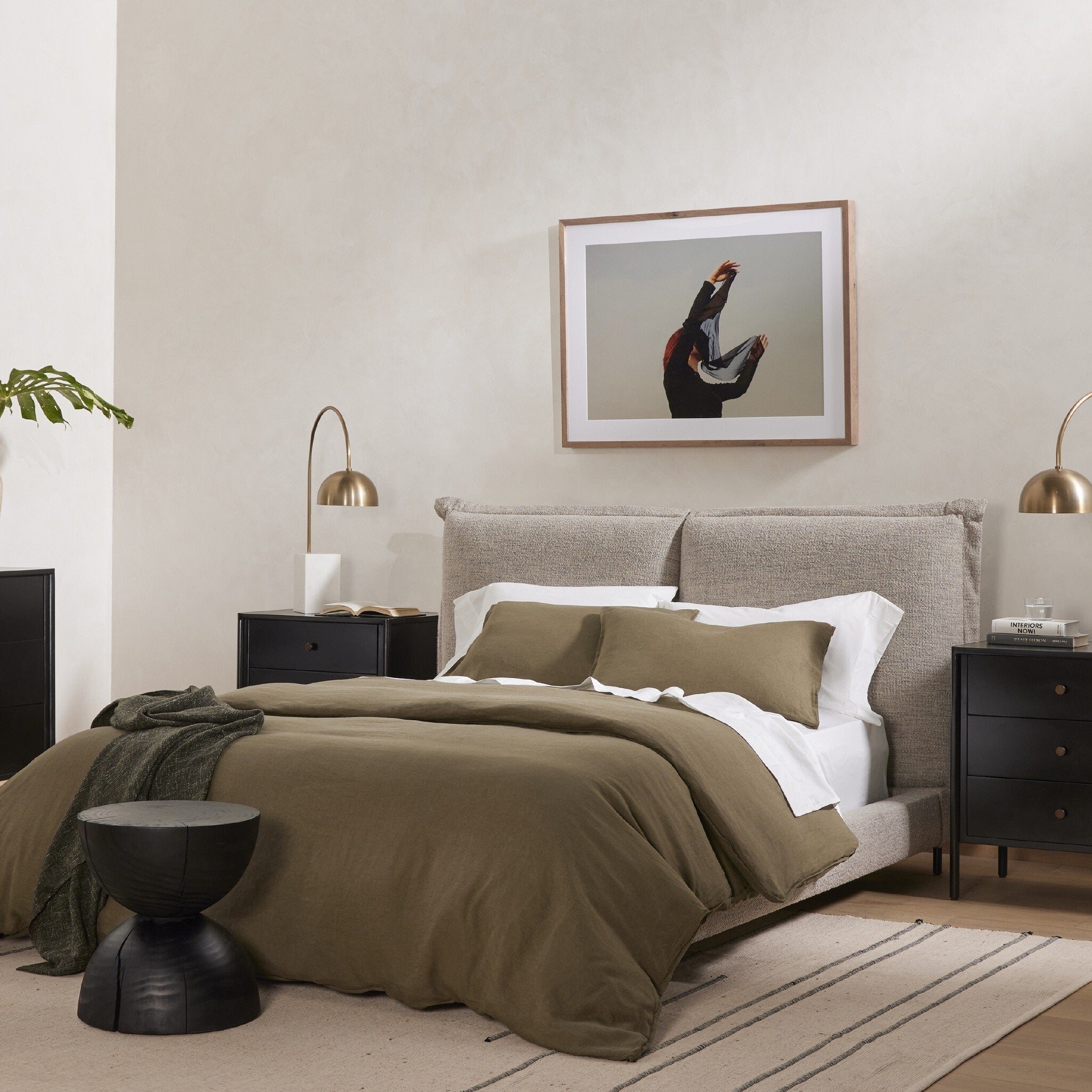 Modern bedroom with an upholstered grey bed, nightstands, and artwork on the wall.