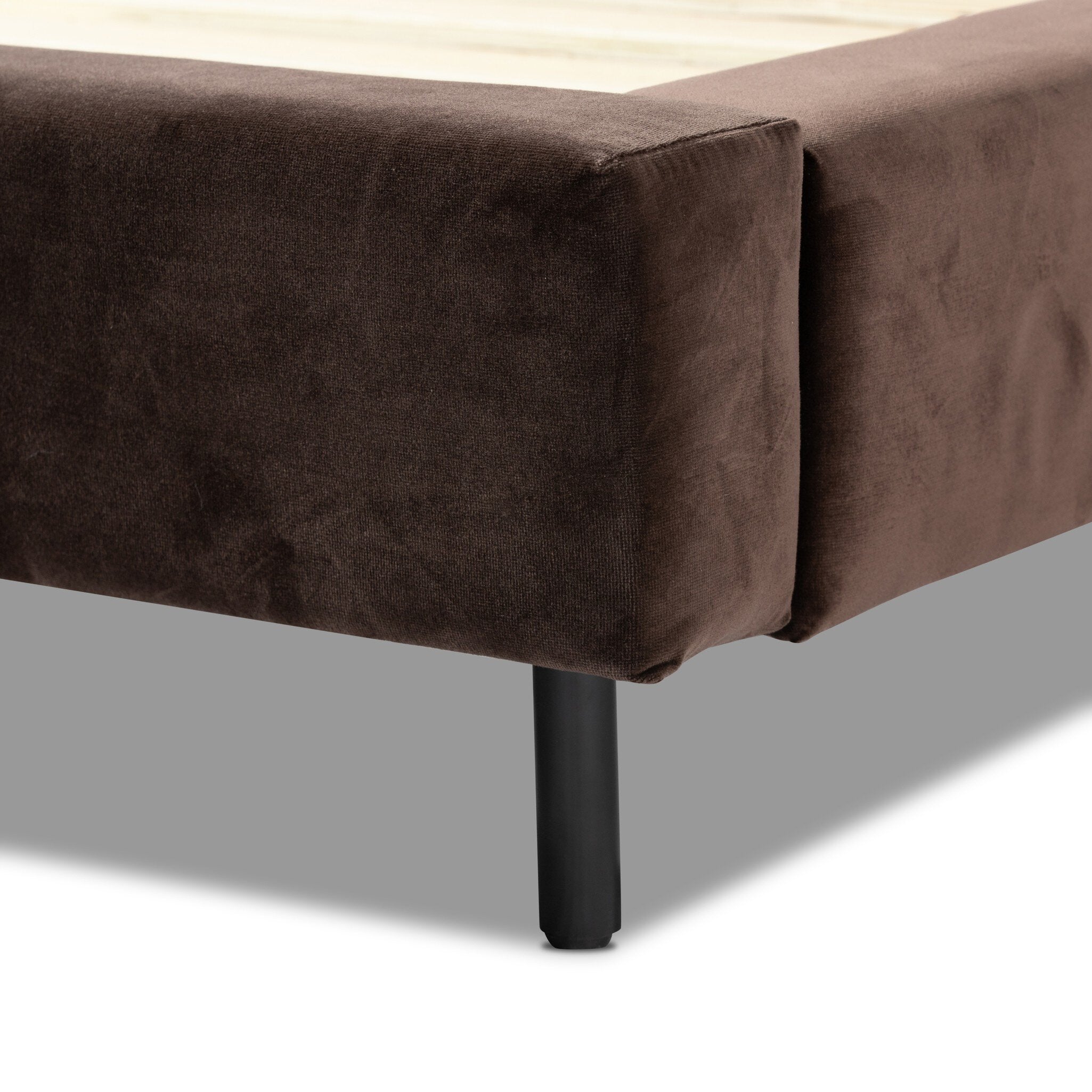 Brown upholstered bench with a black leg on a neutral background
