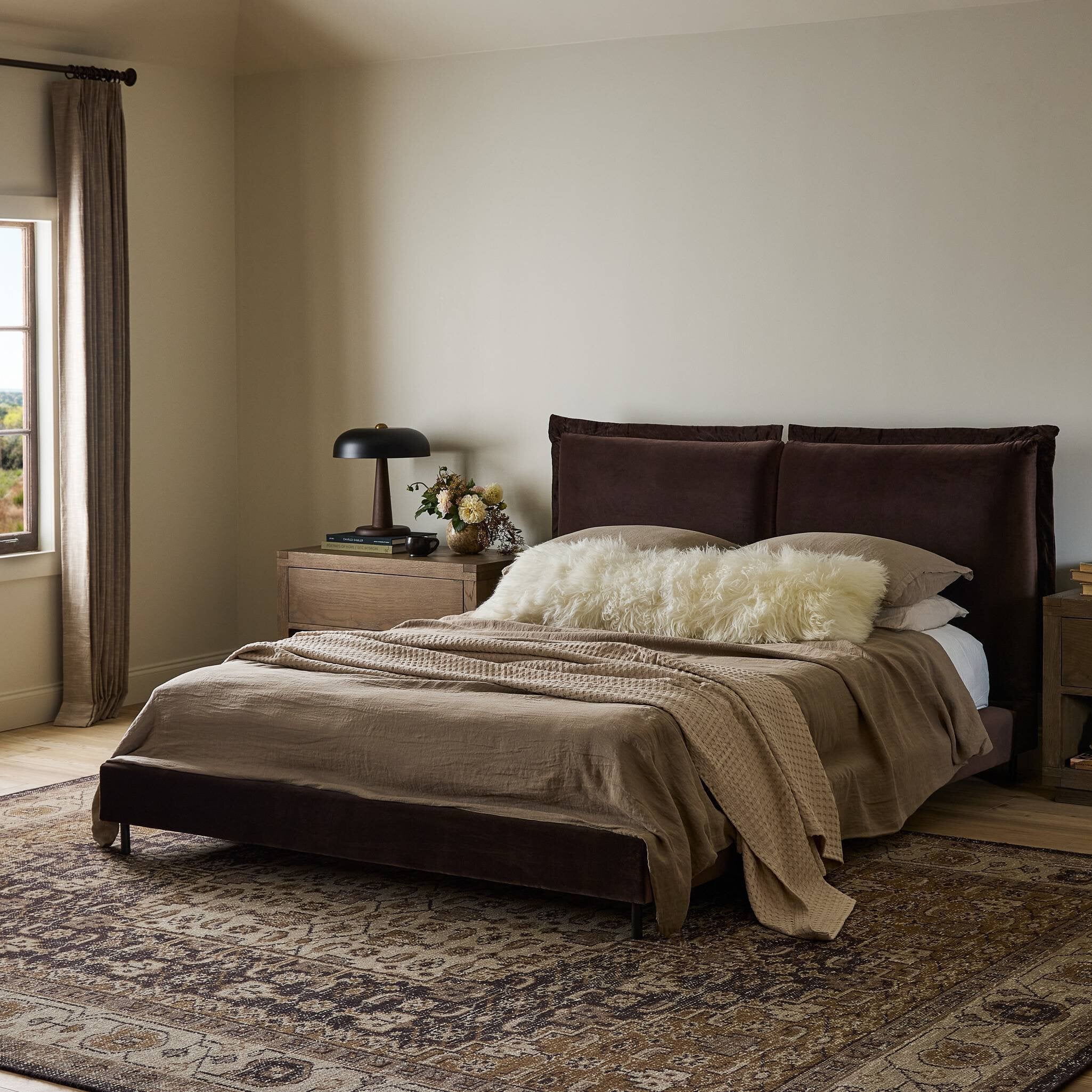 Bedroom with a bed featuring brown bedding and pillows, nightstands with lamps, and a window with curtains.