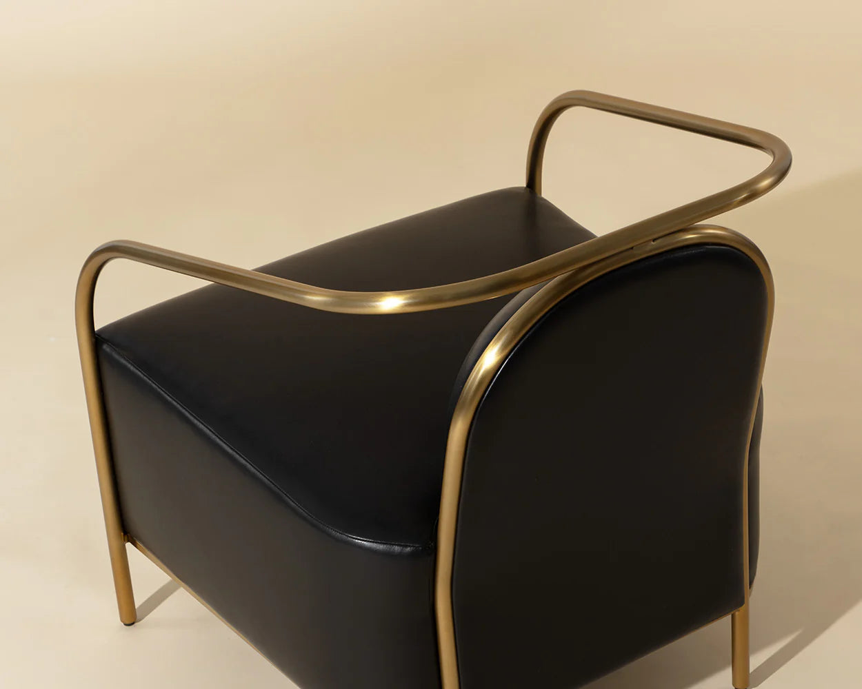 Black leather ottoman with gold metal frame on a beige background