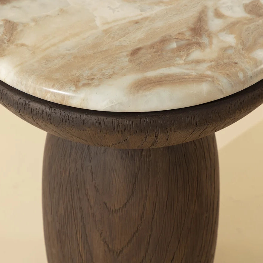 Close-up of a round side table with a polished beige and white marbled top and a dark brown wood-like pedestal base.