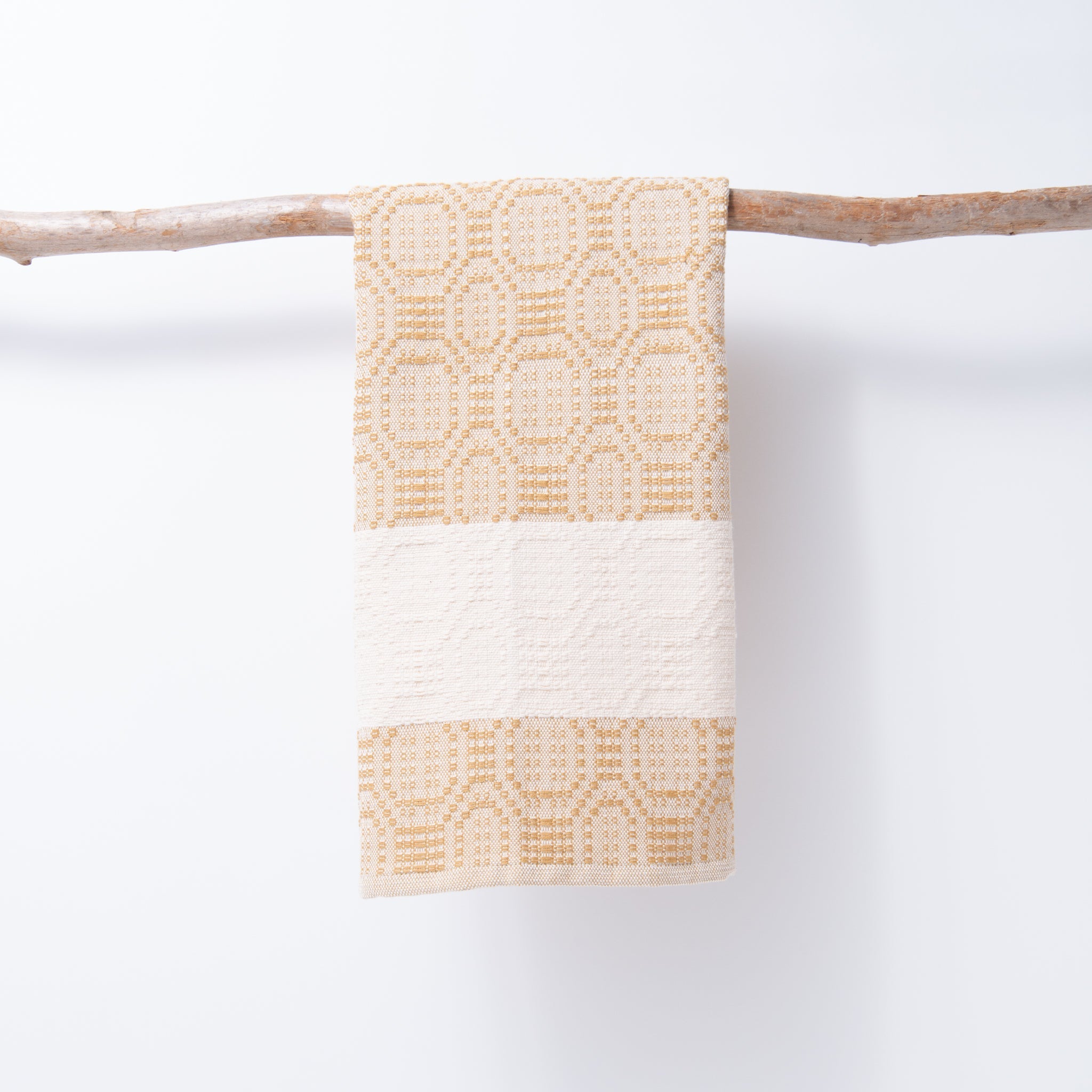 Textured towel with geometric pattern hanging on a branch against a white background