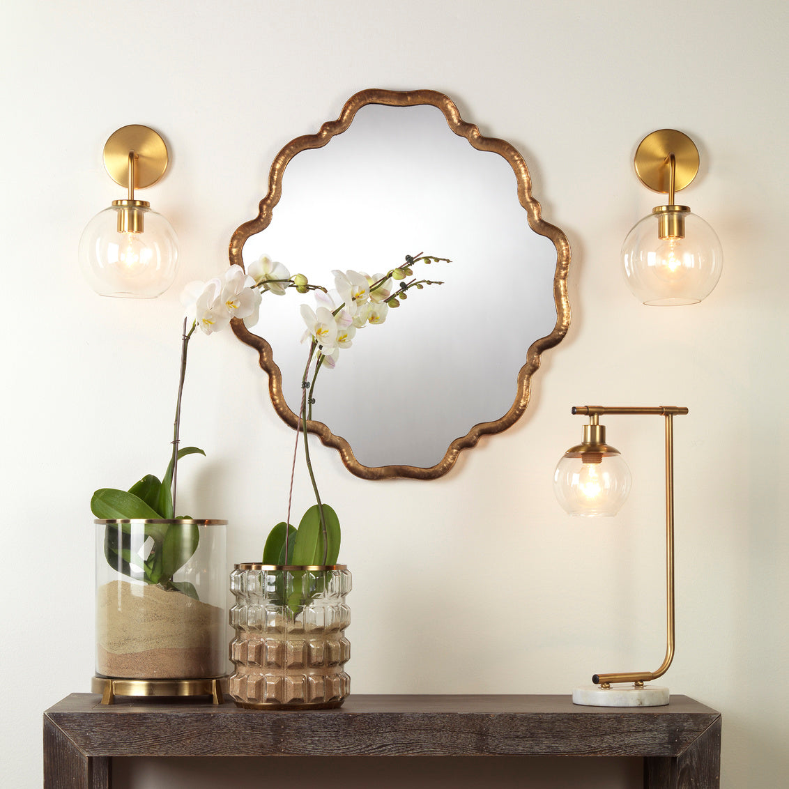 Decorative mirror with gold frame on a wall above a console table with decorative items.
