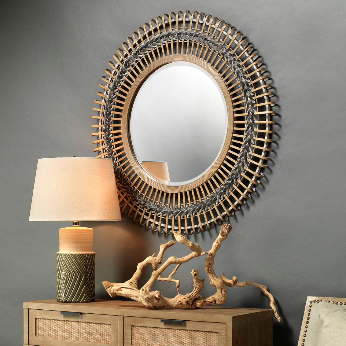 Decorative mirror with bamboo frame on a gray wall above a wooden cabinet with a lamp and decorative piece.