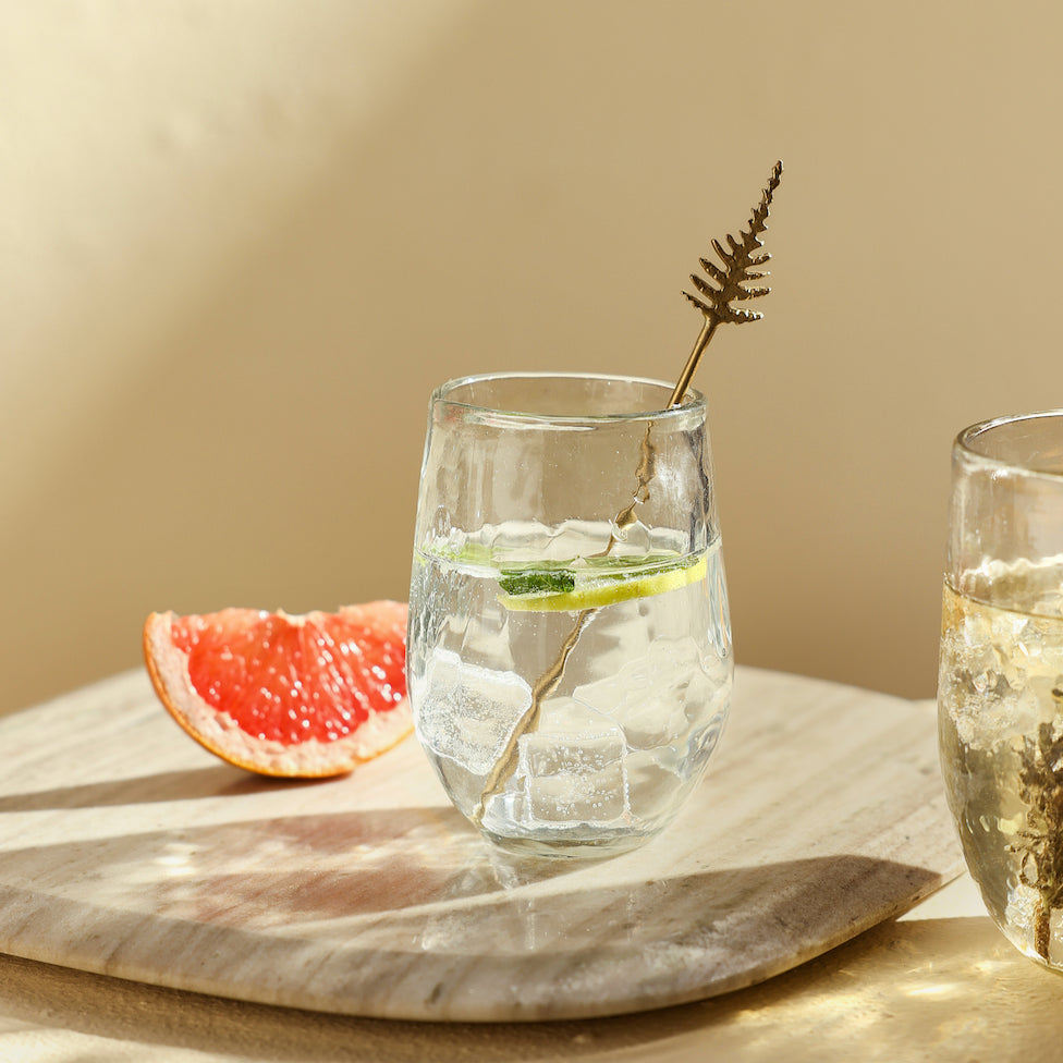 Clear pebbled glass with lemon and ice on a wooden tray with a beige background