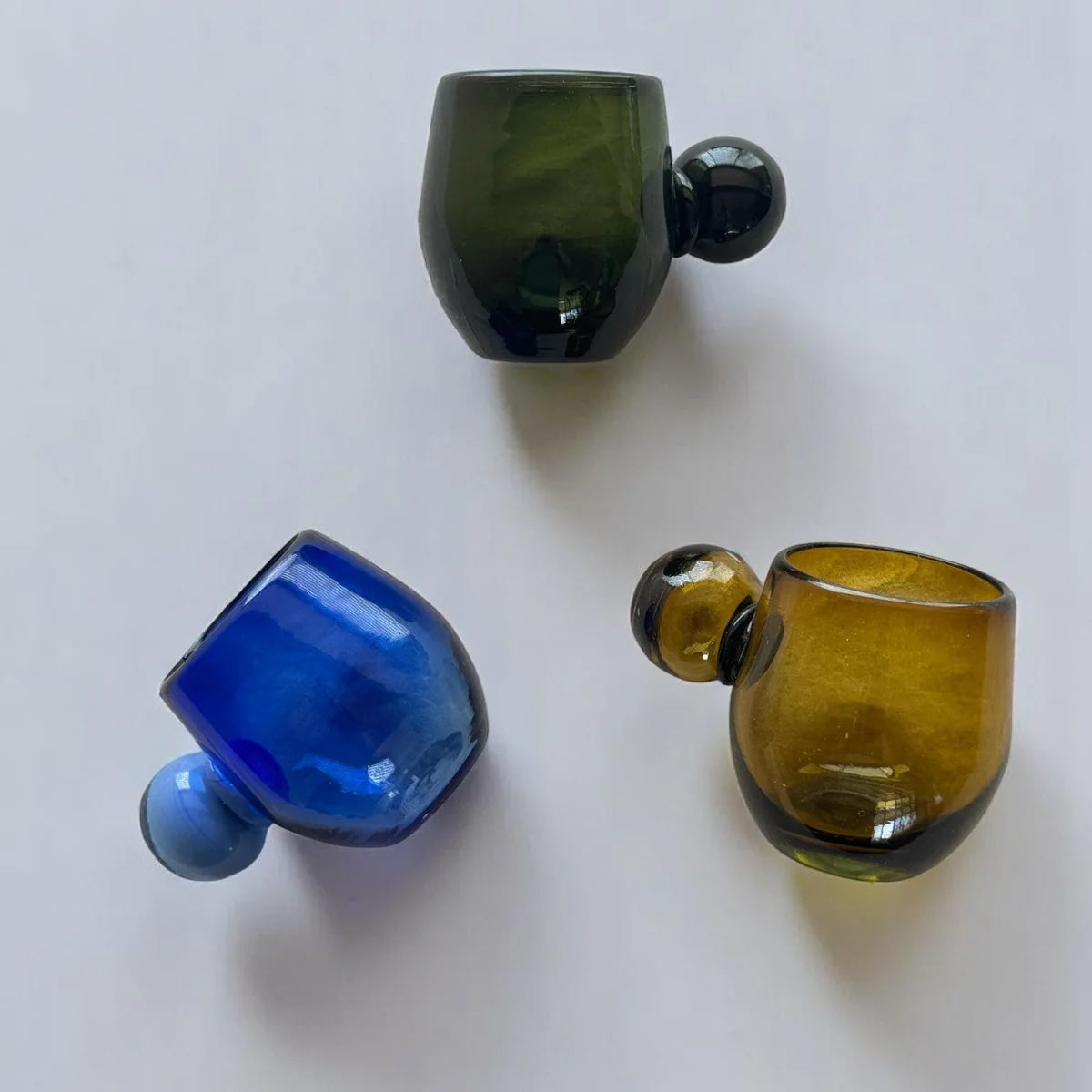 Three glass cups in green, blue, and amber on a white background