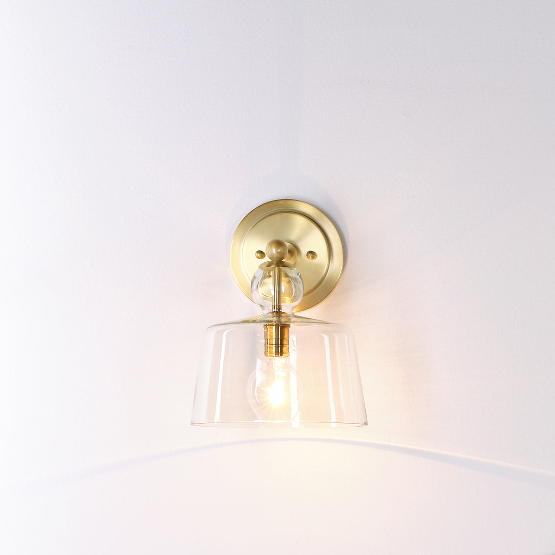 Wall-mounted light fixture with brass finish and clear glass shade on a white background