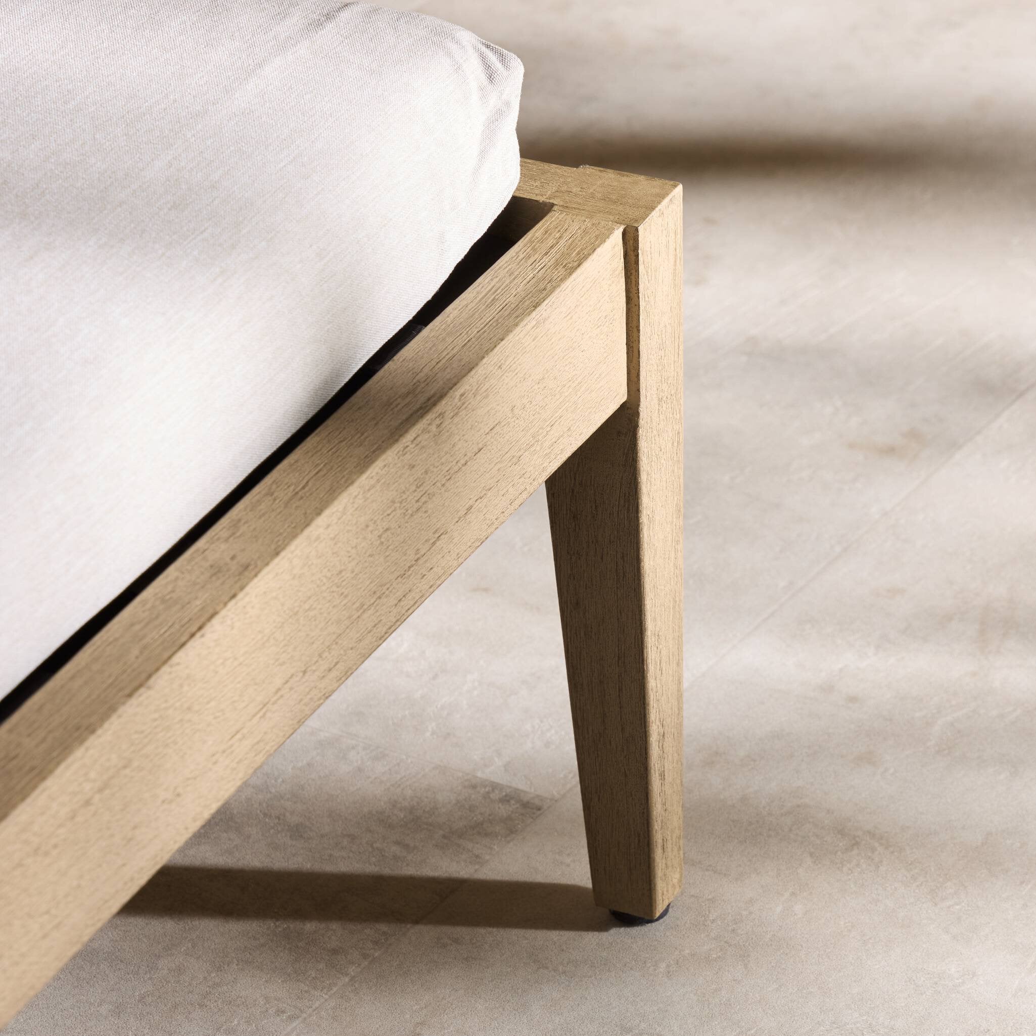 Wooden outdoor chaise frame with a light grey mattress on a neutral background