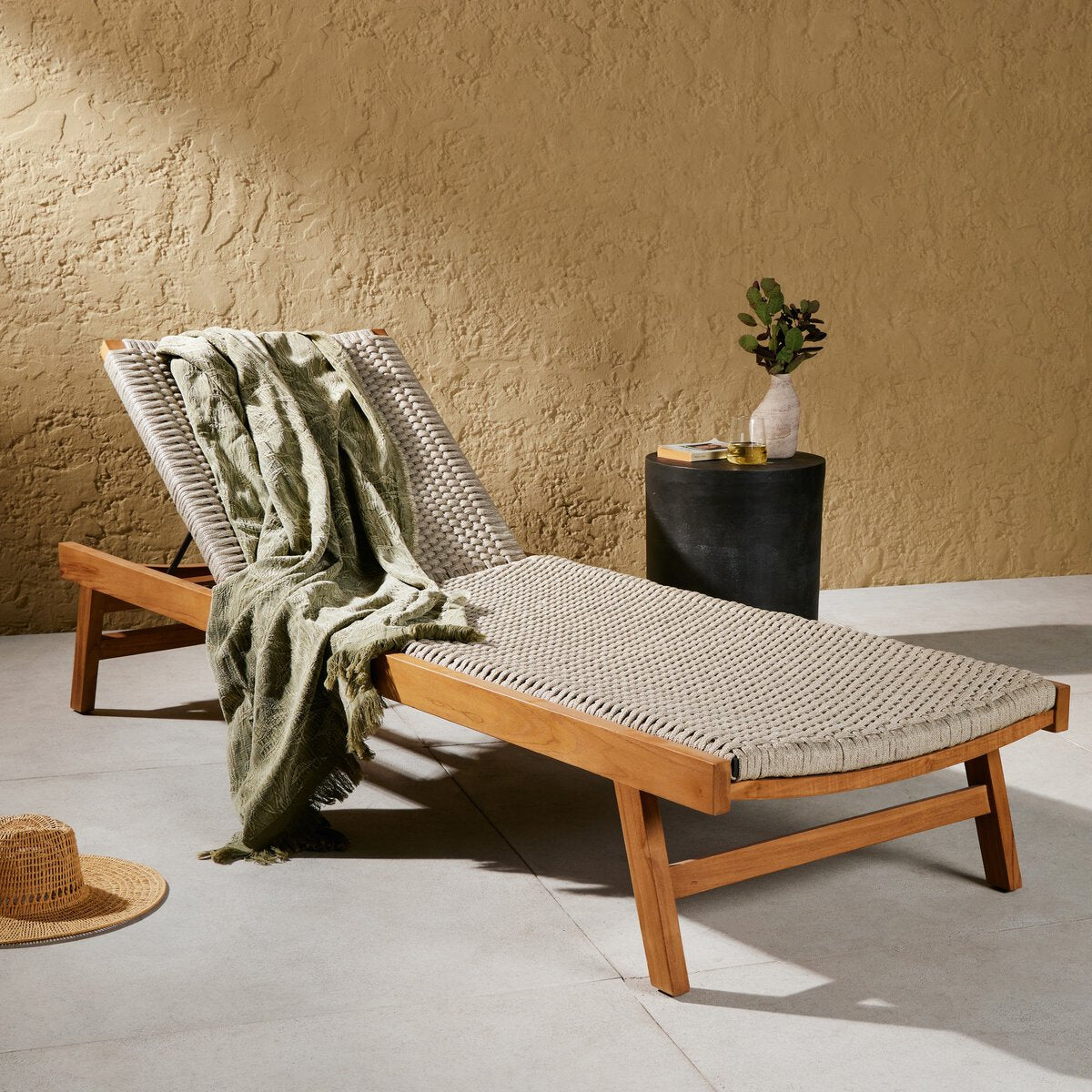 Wooden lounge chair with a green towel draped over it against a beige wall.