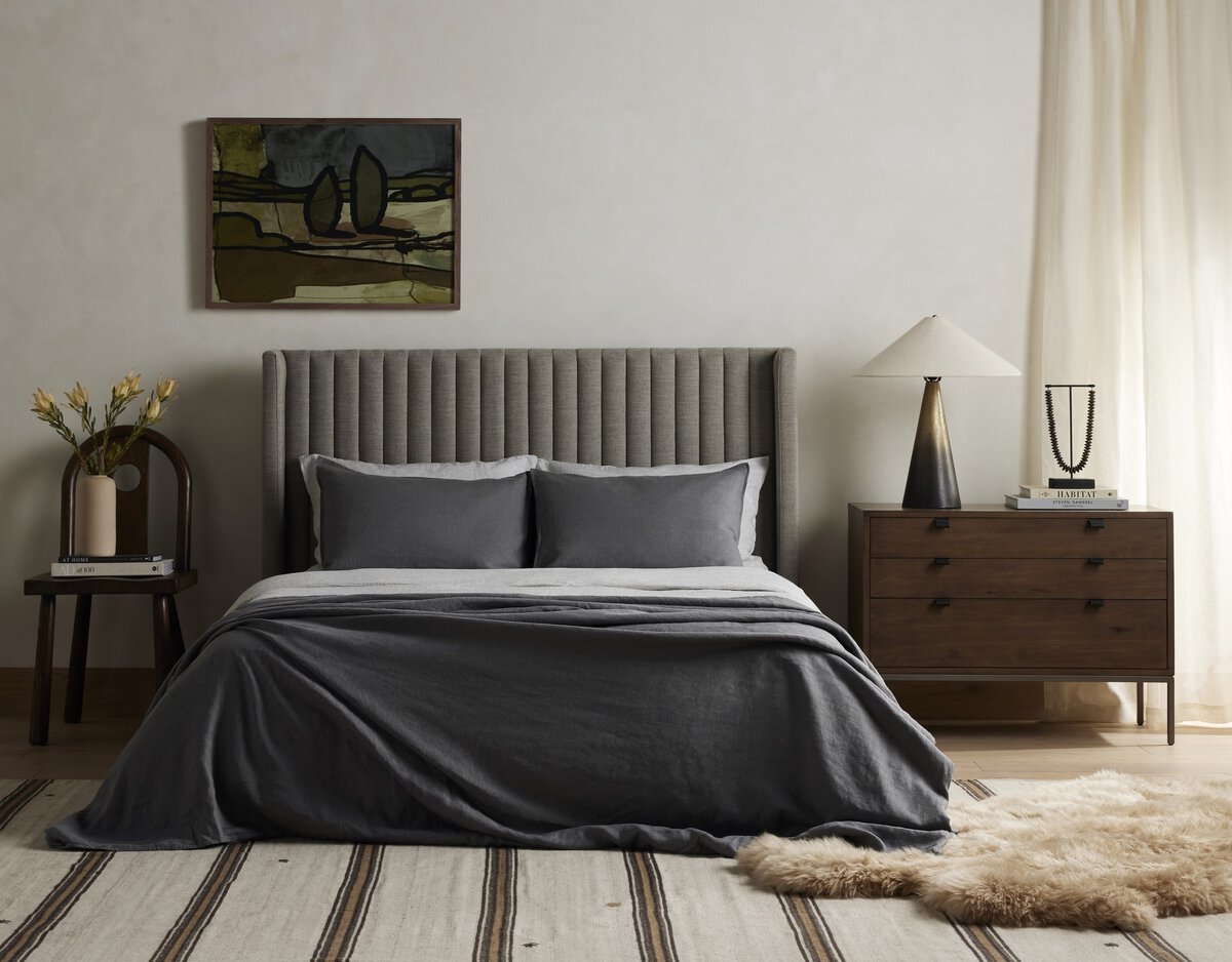 Modern bedroom with gray upholstered bed, wooden nightstands, and abstract painting on wall.