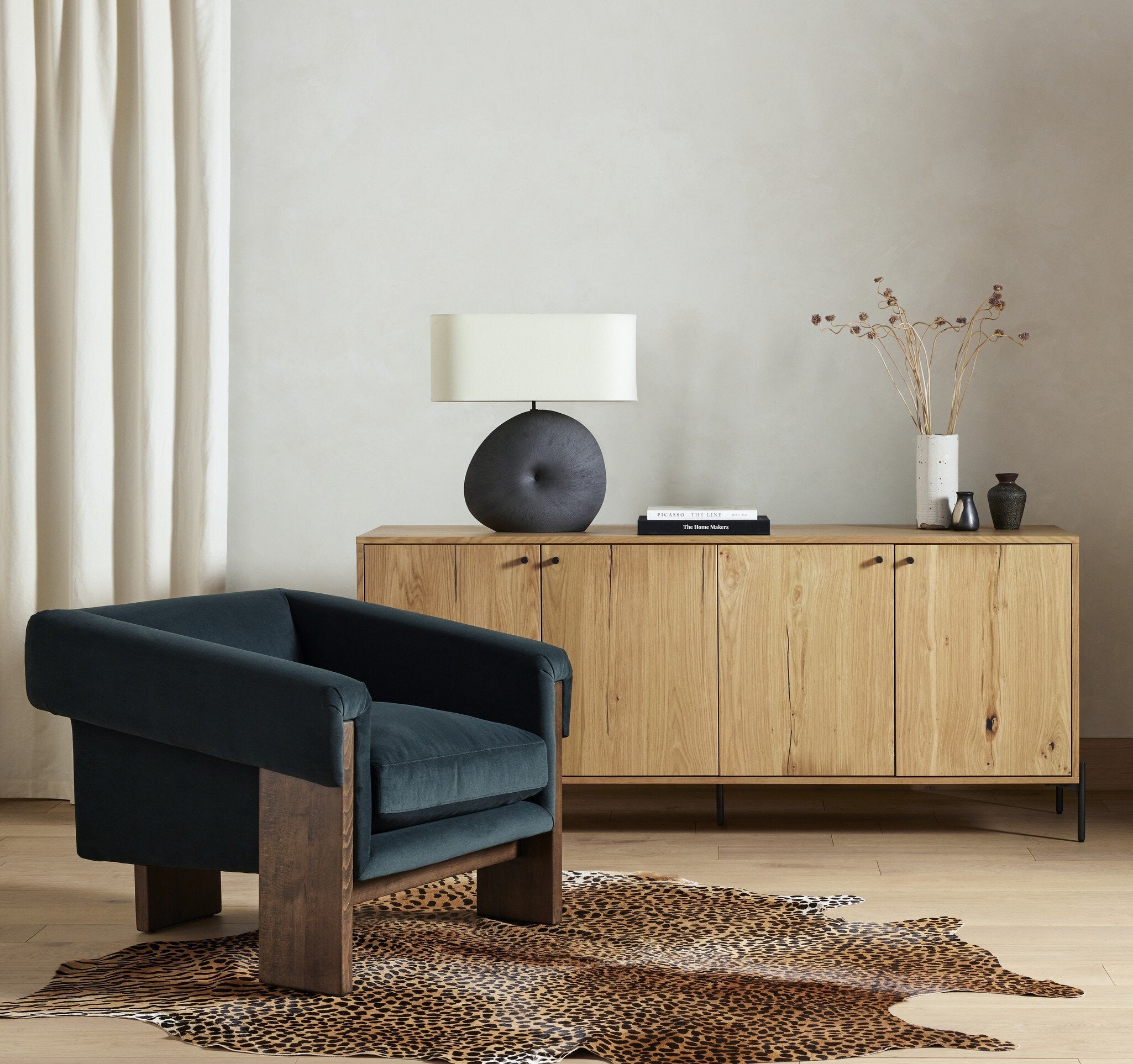 Modern living room with a dark blue armchair, wooden sideboard, and decorative lamp.