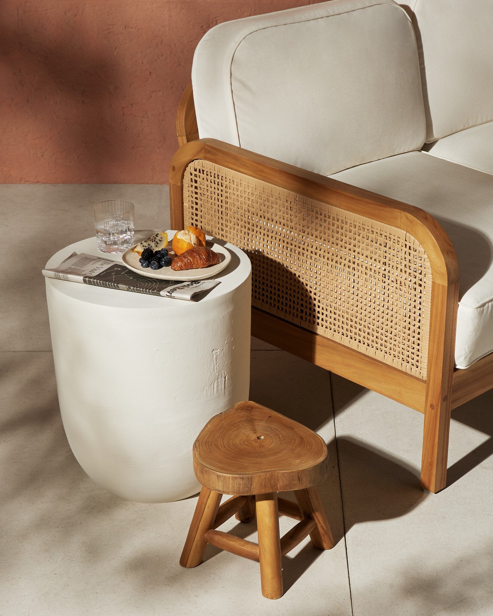 White side table with a plate of food next to a wooden chair with wicker backrest.