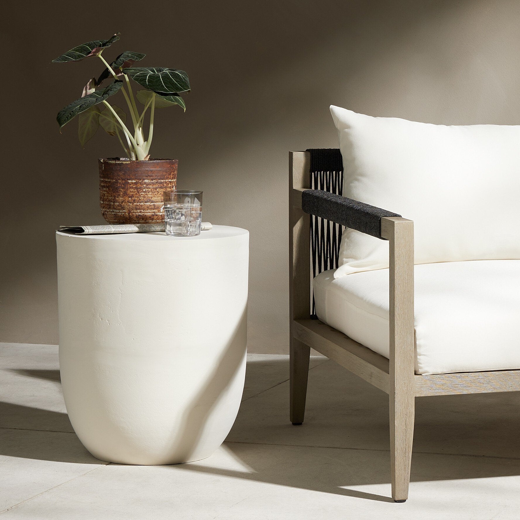 White side table with a plant and glass, next to a wooden chair with white cushions.