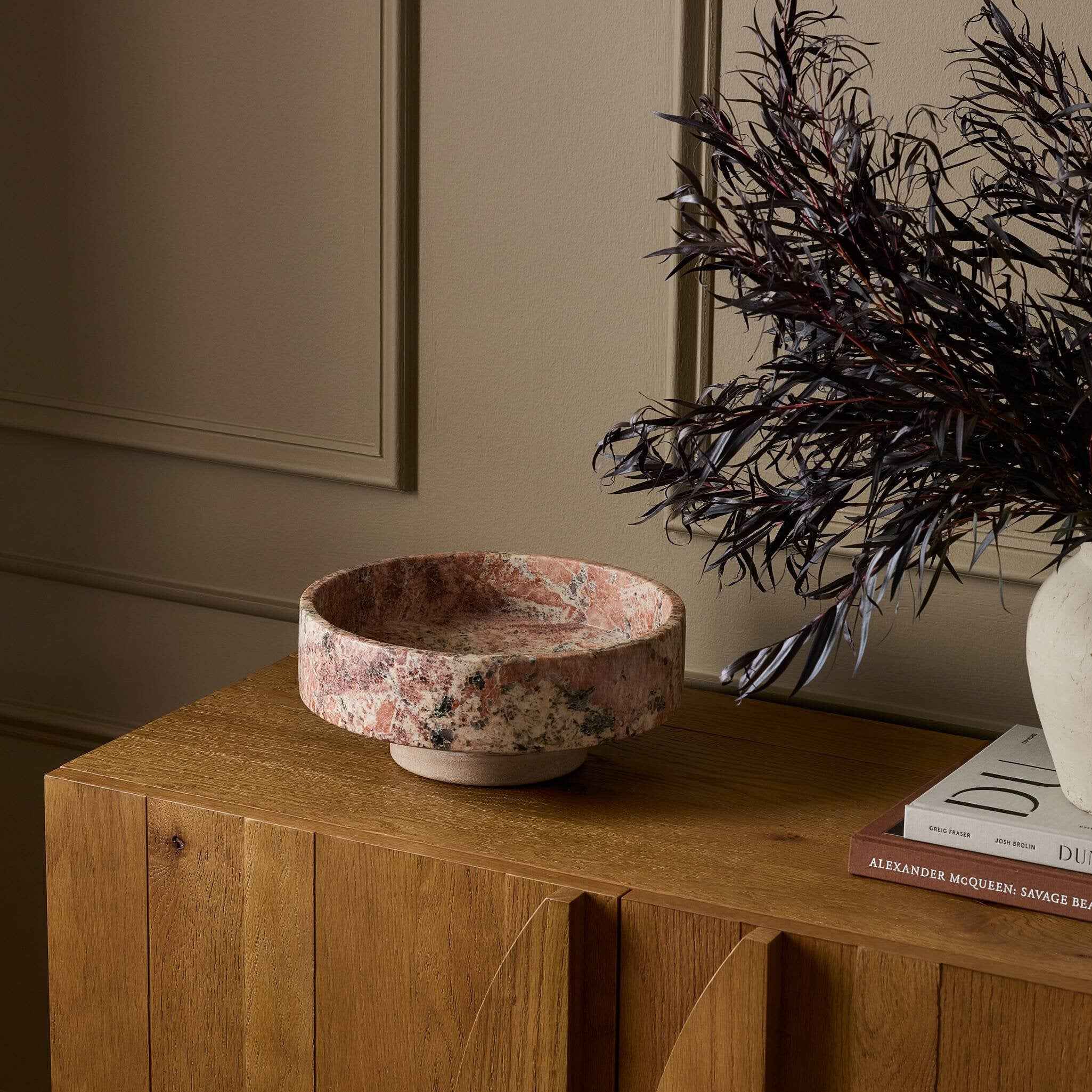 Decorative bowl on a wooden surface with a plant and books in the background