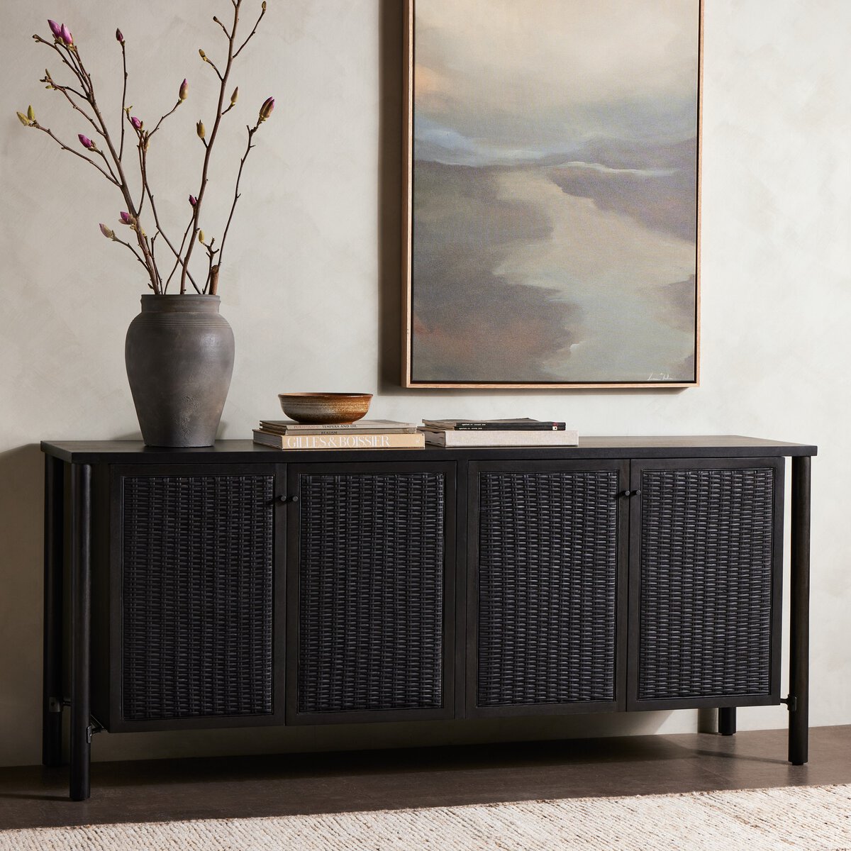Black wicker sideboard with decorative items in a room with a painting on the wall.