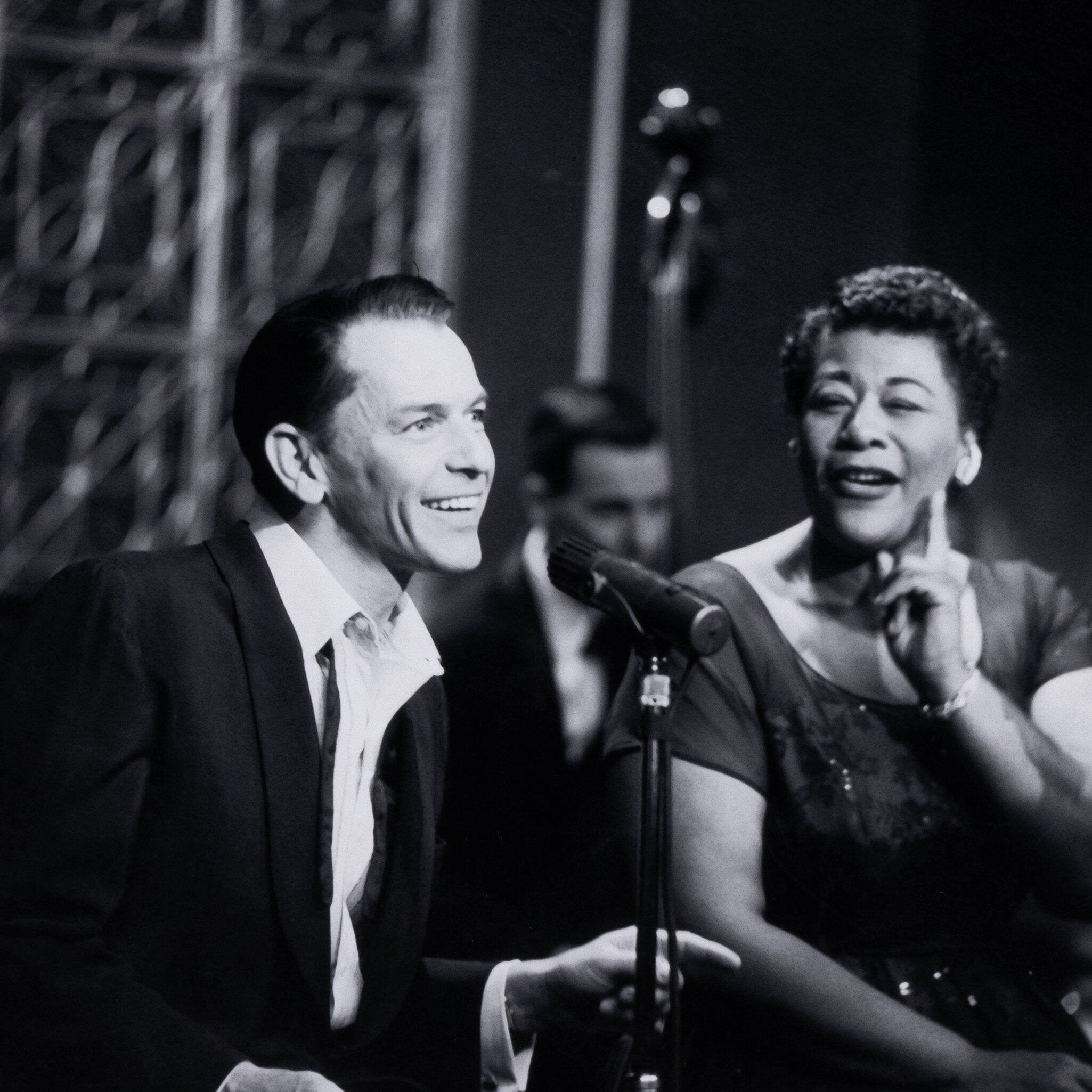 Black and white photo of Sinatra and Fitzgerald sitting next to microphones on a stage.