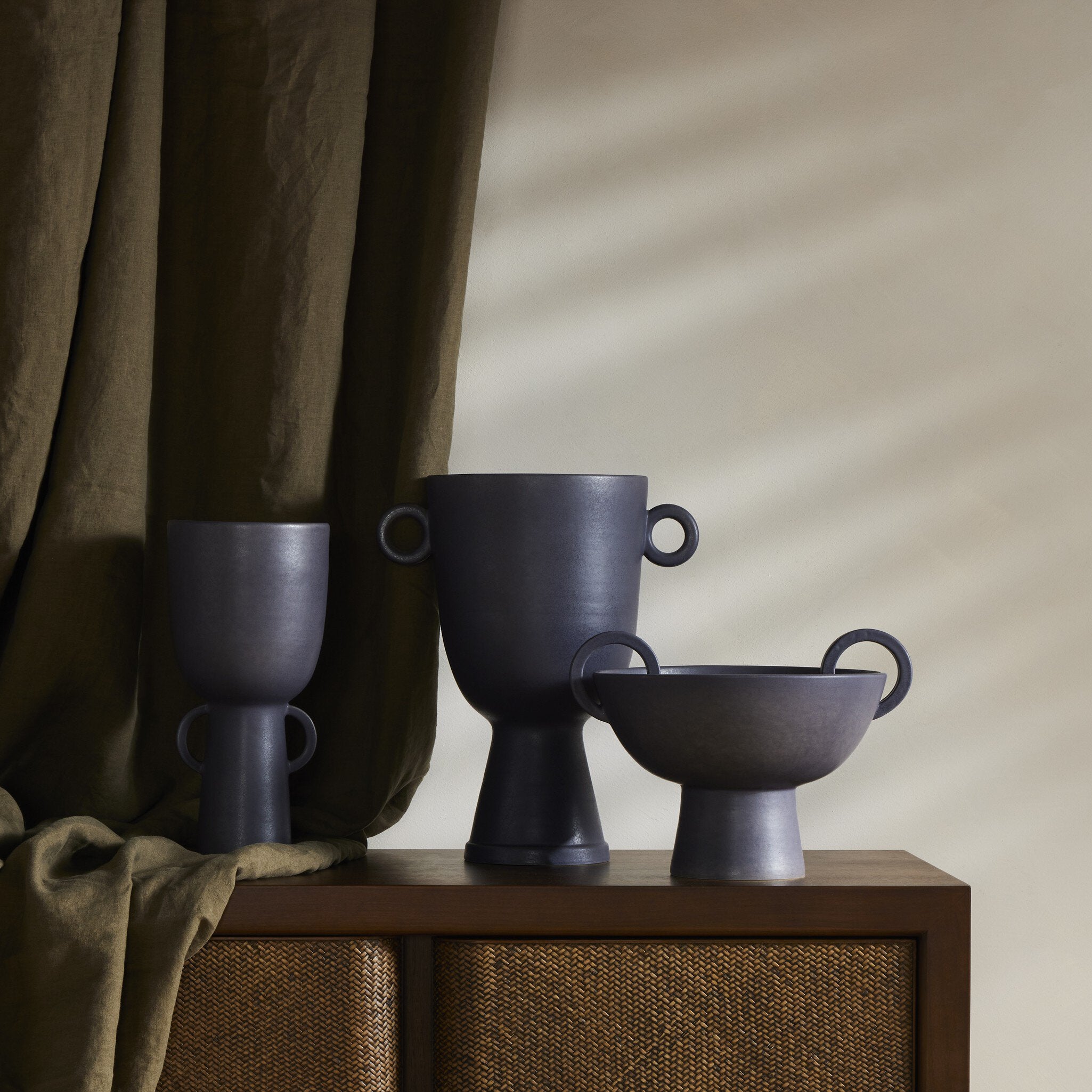 Three dark gray ceramic vases on a wooden surface with a neutral background