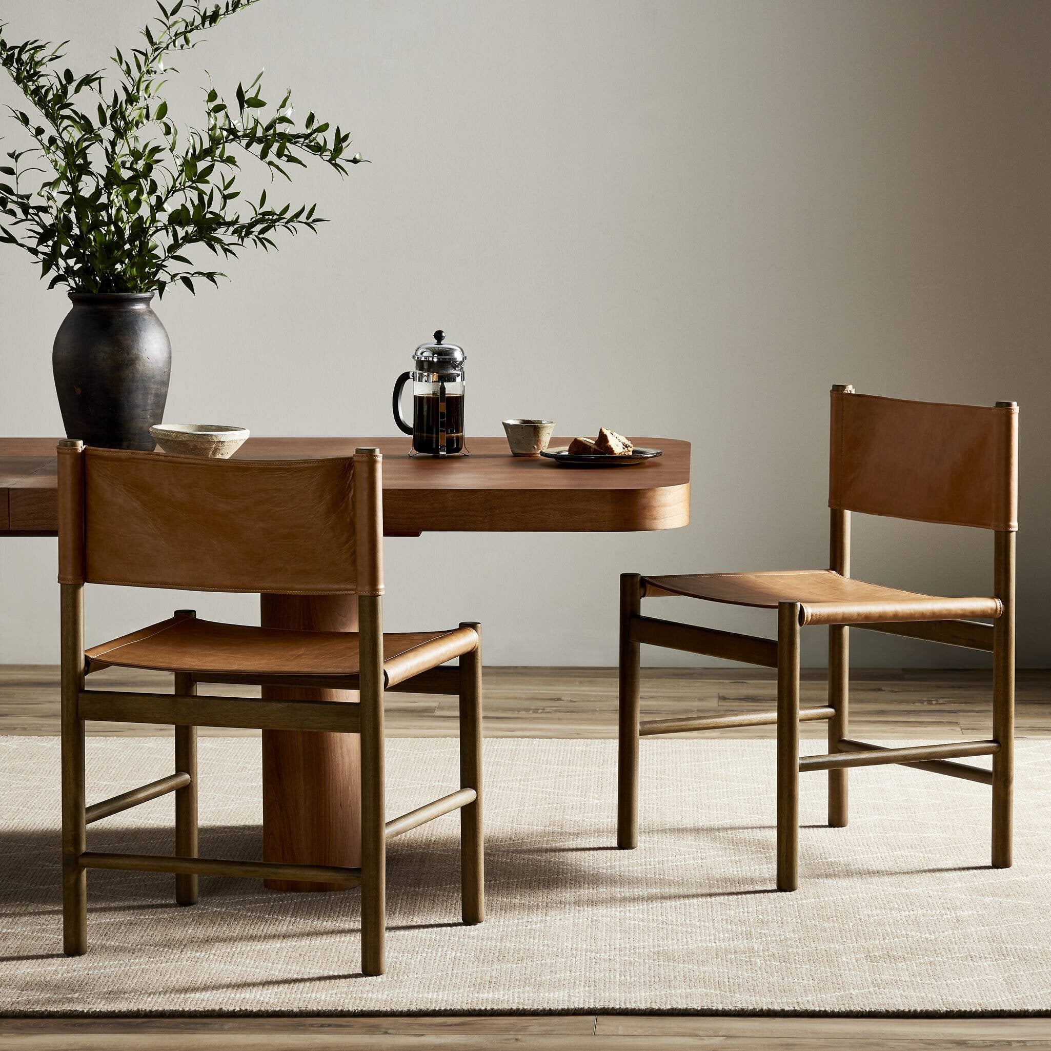 Dining table with chairs and a vase of plants in a room.