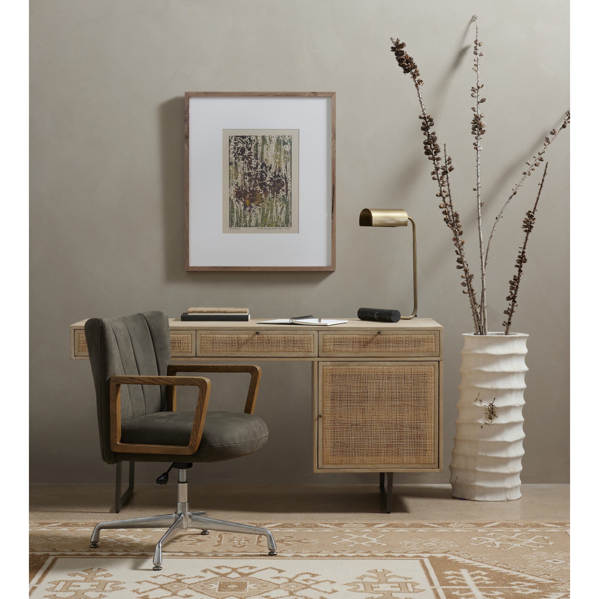 Home office with wooden desk, gray chair, framed artwork, and decorative vase.