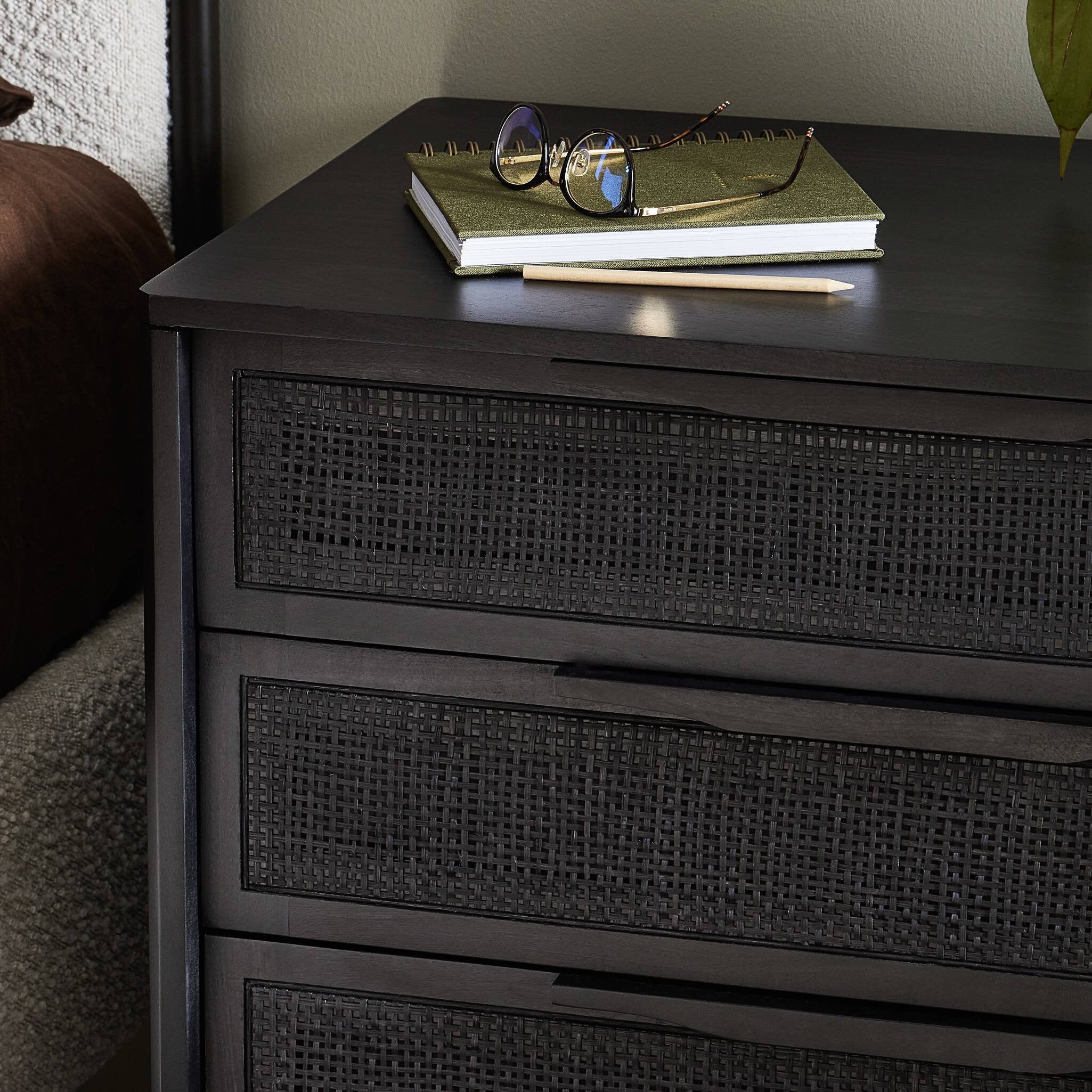 Dark wooden dresser with wicker-like texture, notebook, and glasses on top.