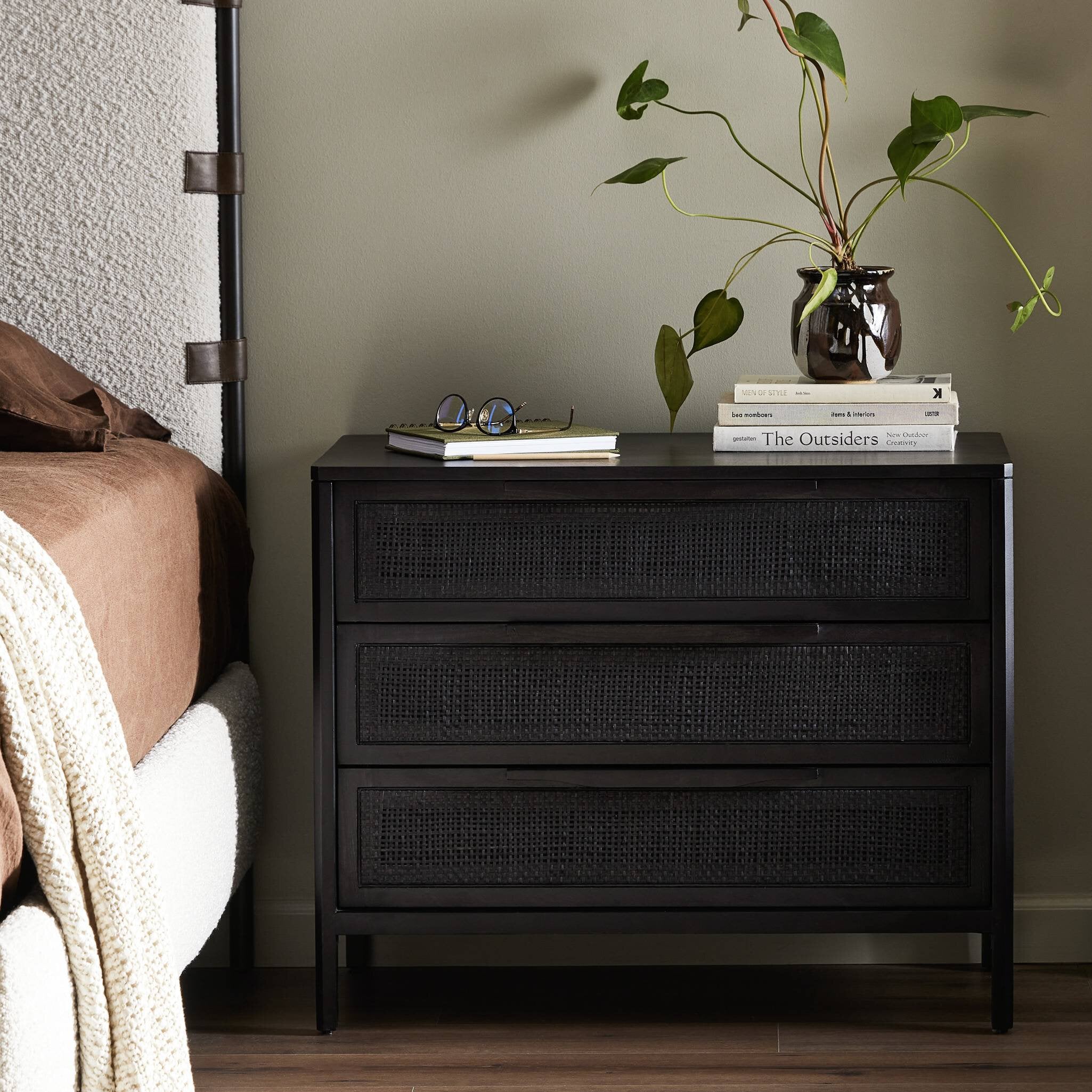 Black wicker nightstand with books and a plant in a bedroom setting