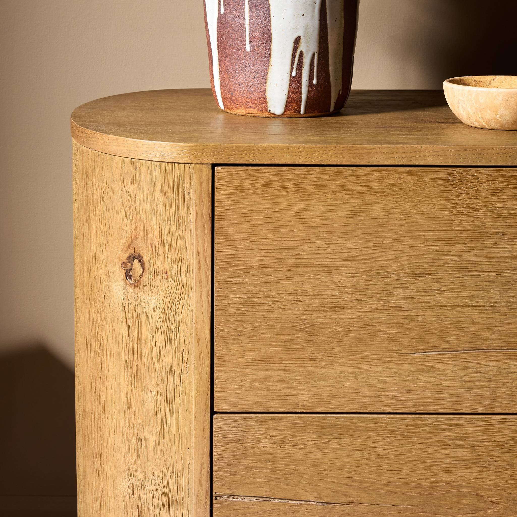 Wooden dresser with two drawers and a ceramic vase on top against a beige wall.