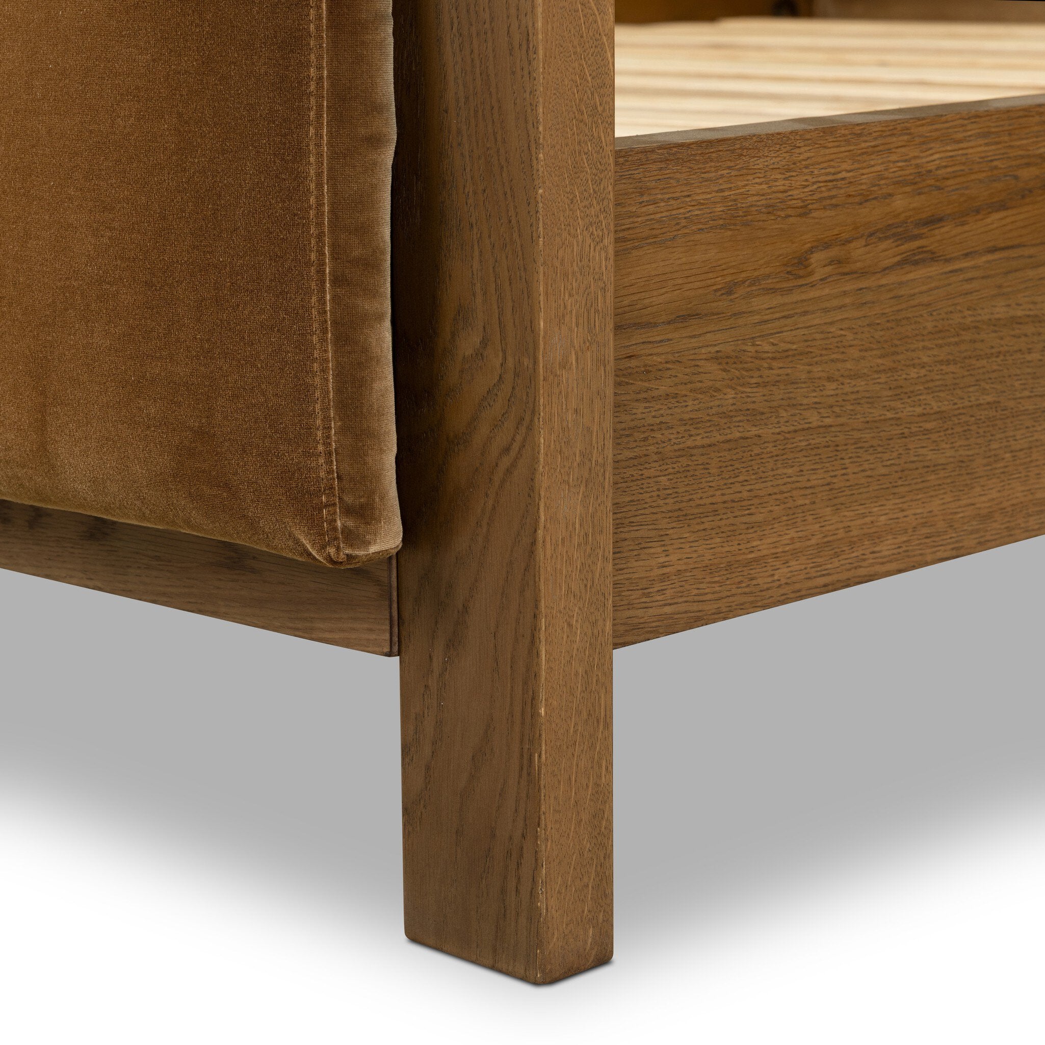 Close-up of a wooden bedframe with brown cushioned footboard on a gray background