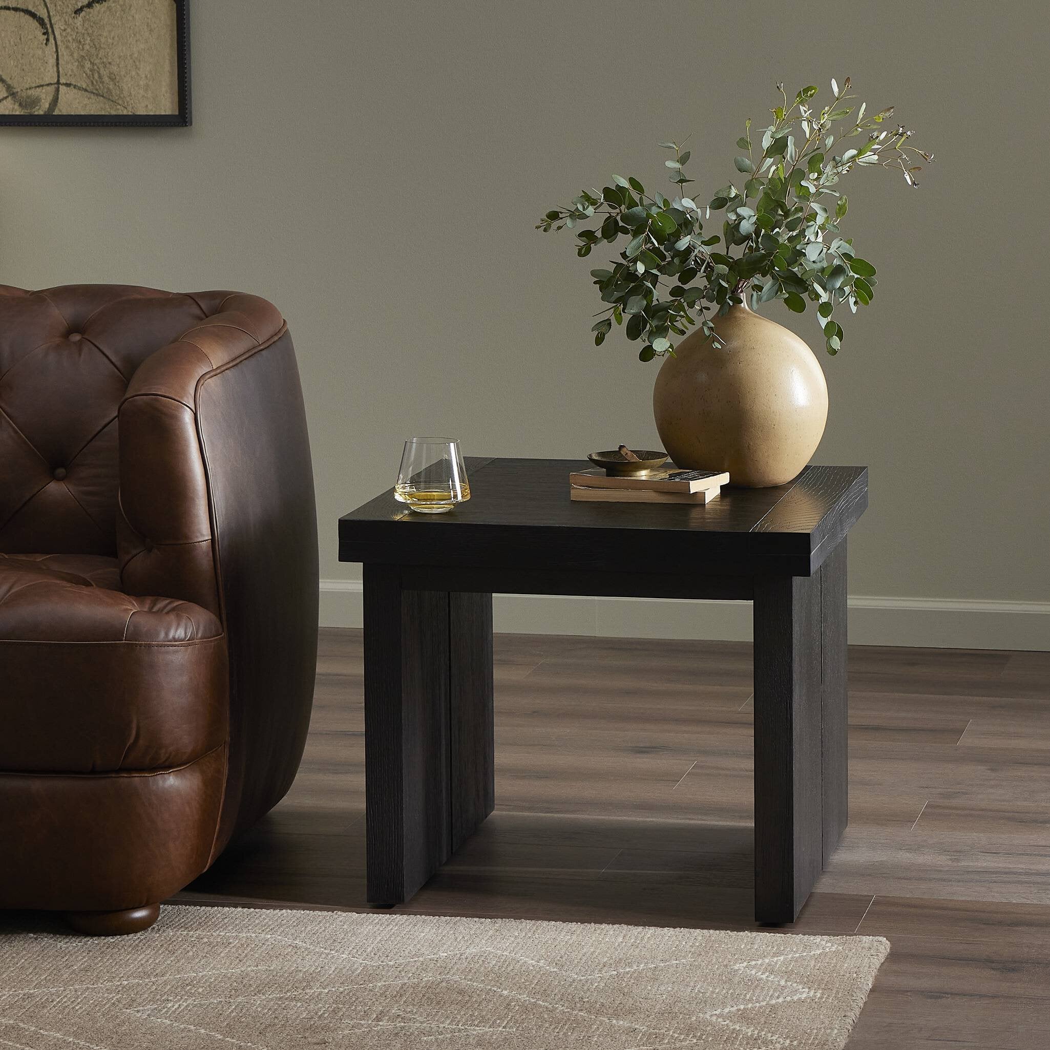 Living room with a brown leather armchair and a dark wooden side table with a vase and glass.
