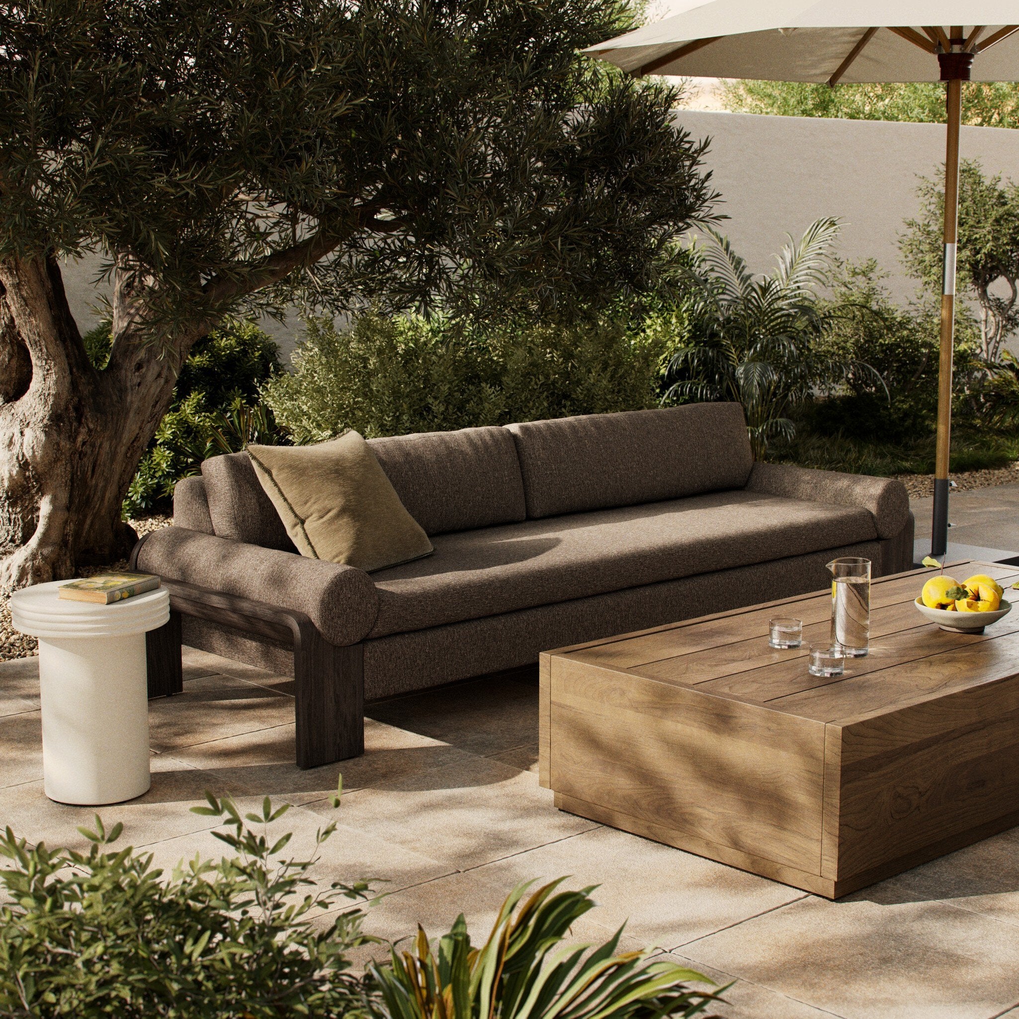 Outdoor patio with brown sofa, wooden coffee table, and umbrella in a garden setting.