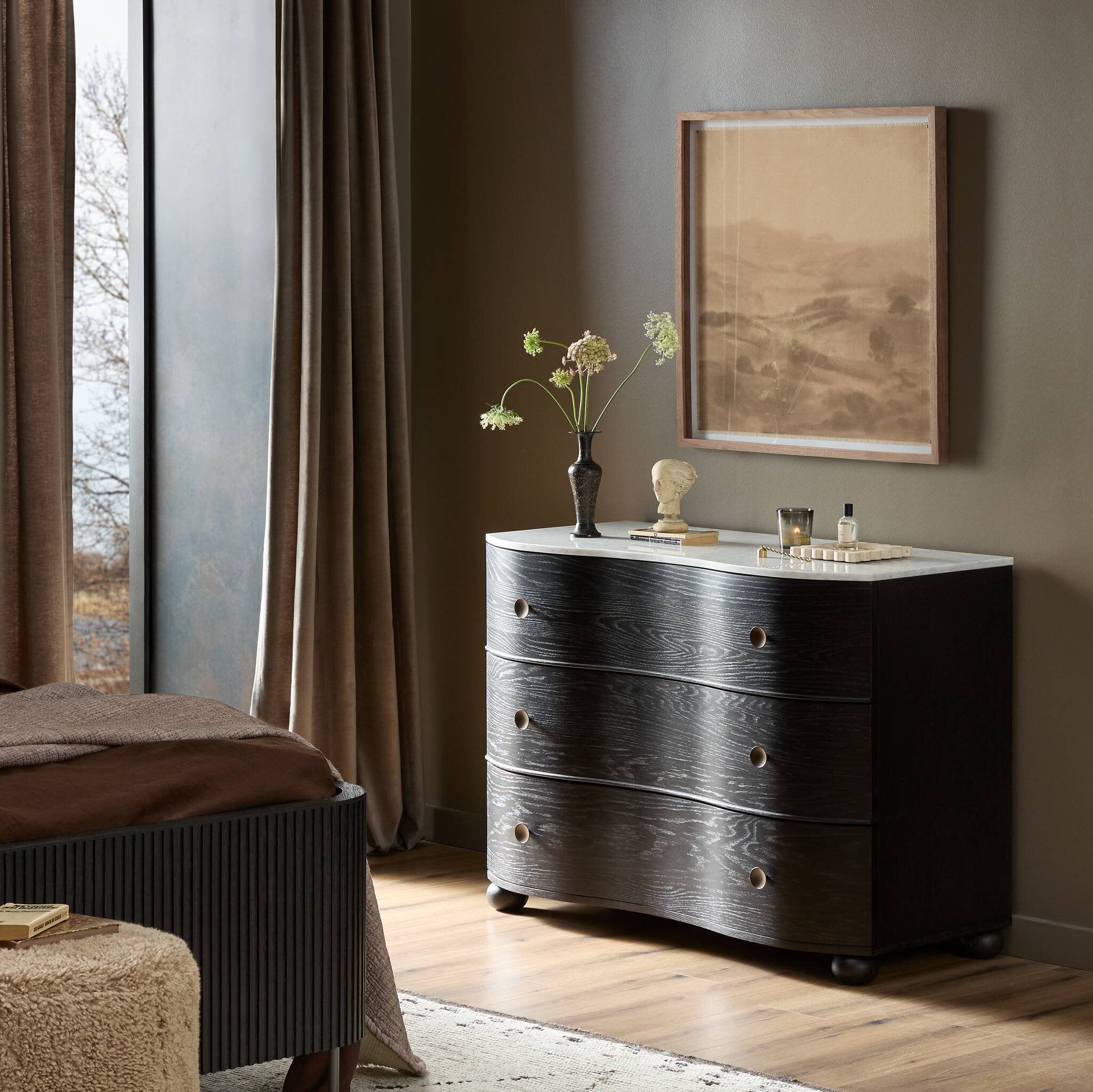 Dark wooden dresser with decorative items in a room with a window and framed picture on the wall.
