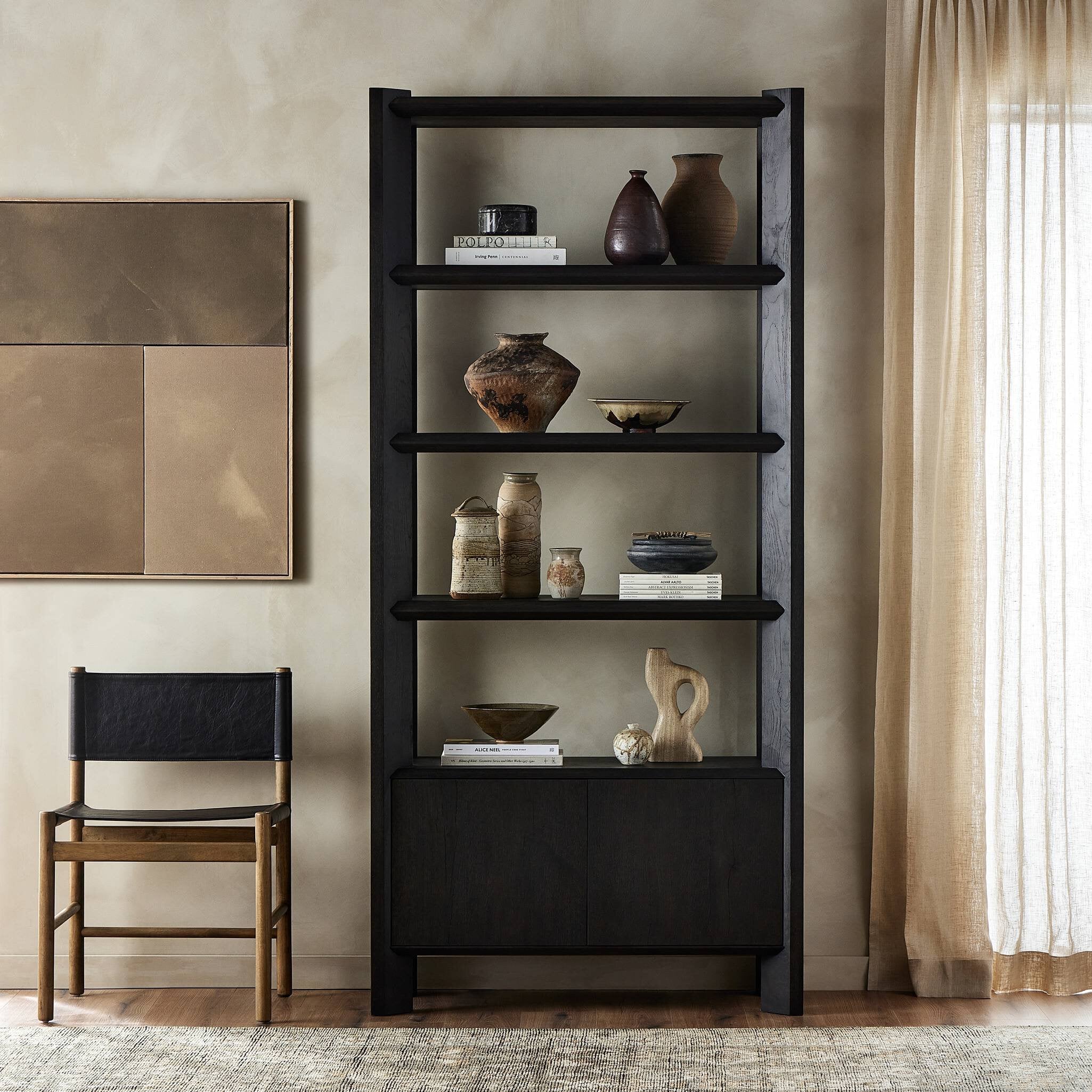 Black bookshelf with decorative items in a room with a chair and window.