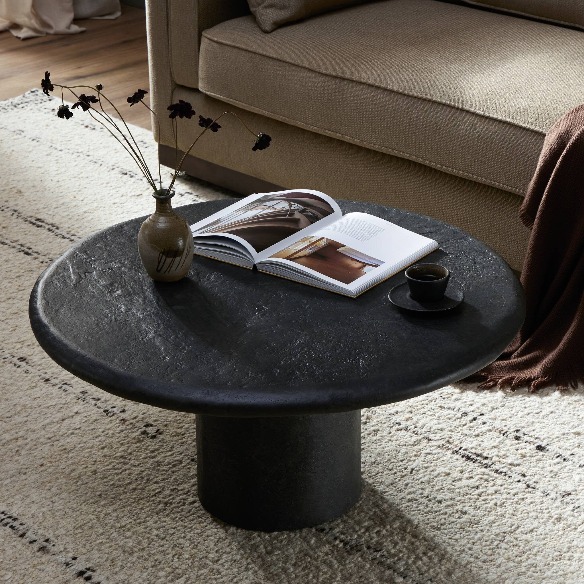 Black concrete table with a vase, book, and cup in a living room setting.