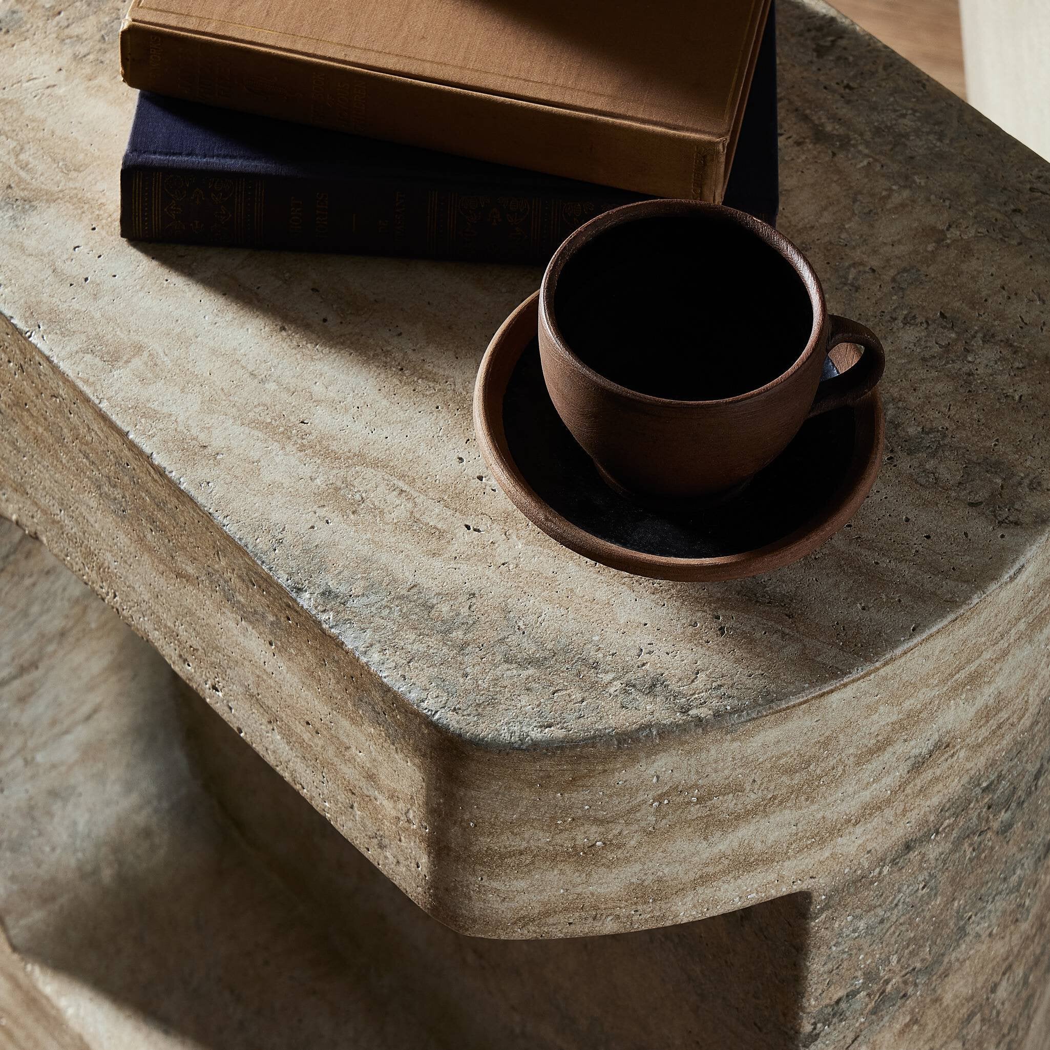 Brown ceramic cup and saucer on a faux stone surface with a box in the background