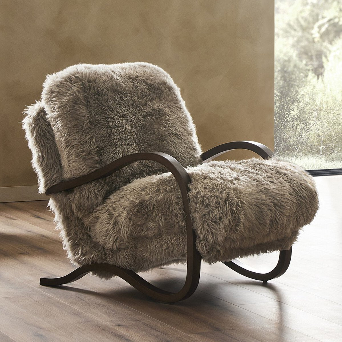 Fluffy gray armchair on a wooden floor with a neutral wall and window in the background
