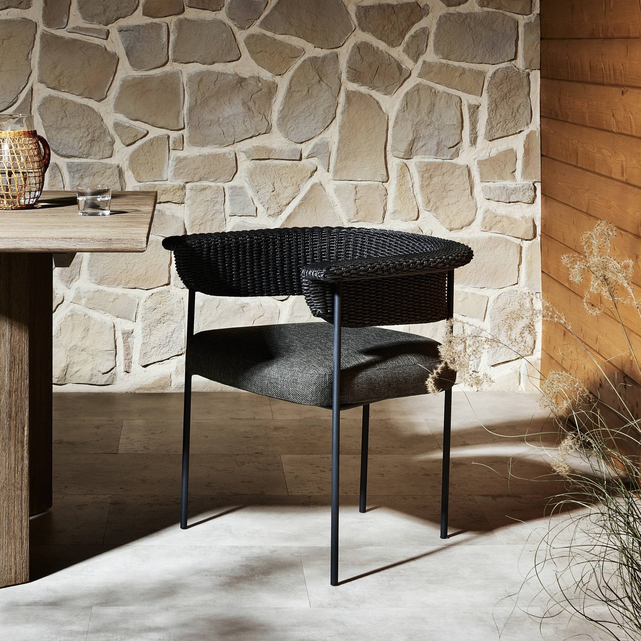 Wicker chair against a stone wall with a wooden table and decorative elements.