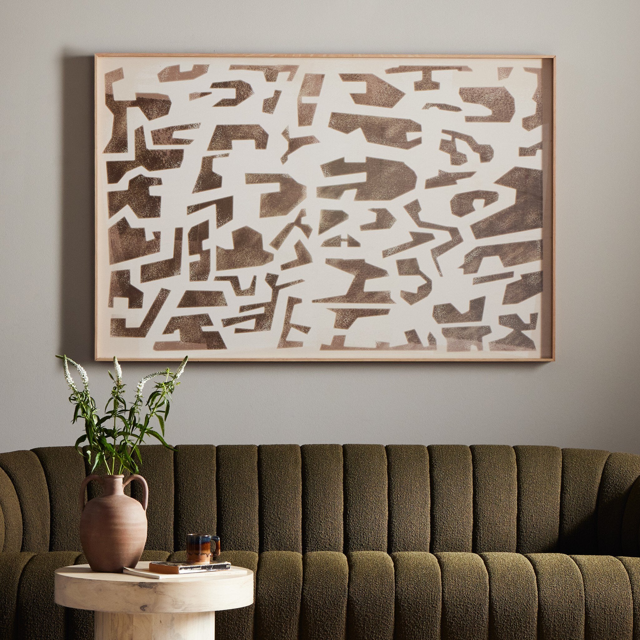 Abstract wall art above a green sofa with a small table and plant.