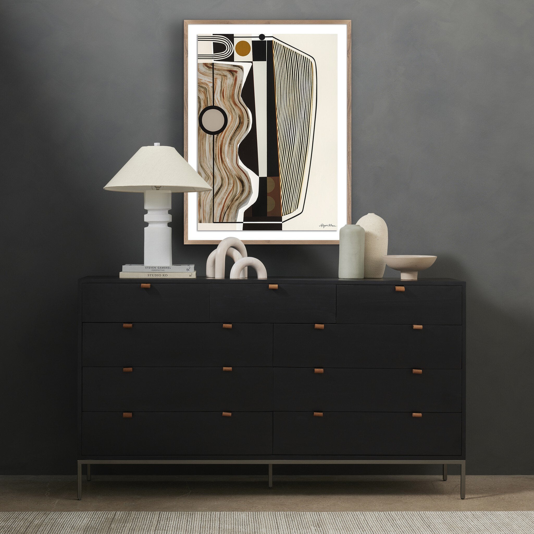 Black dresser with decorative items against a gray wall with abstract art.