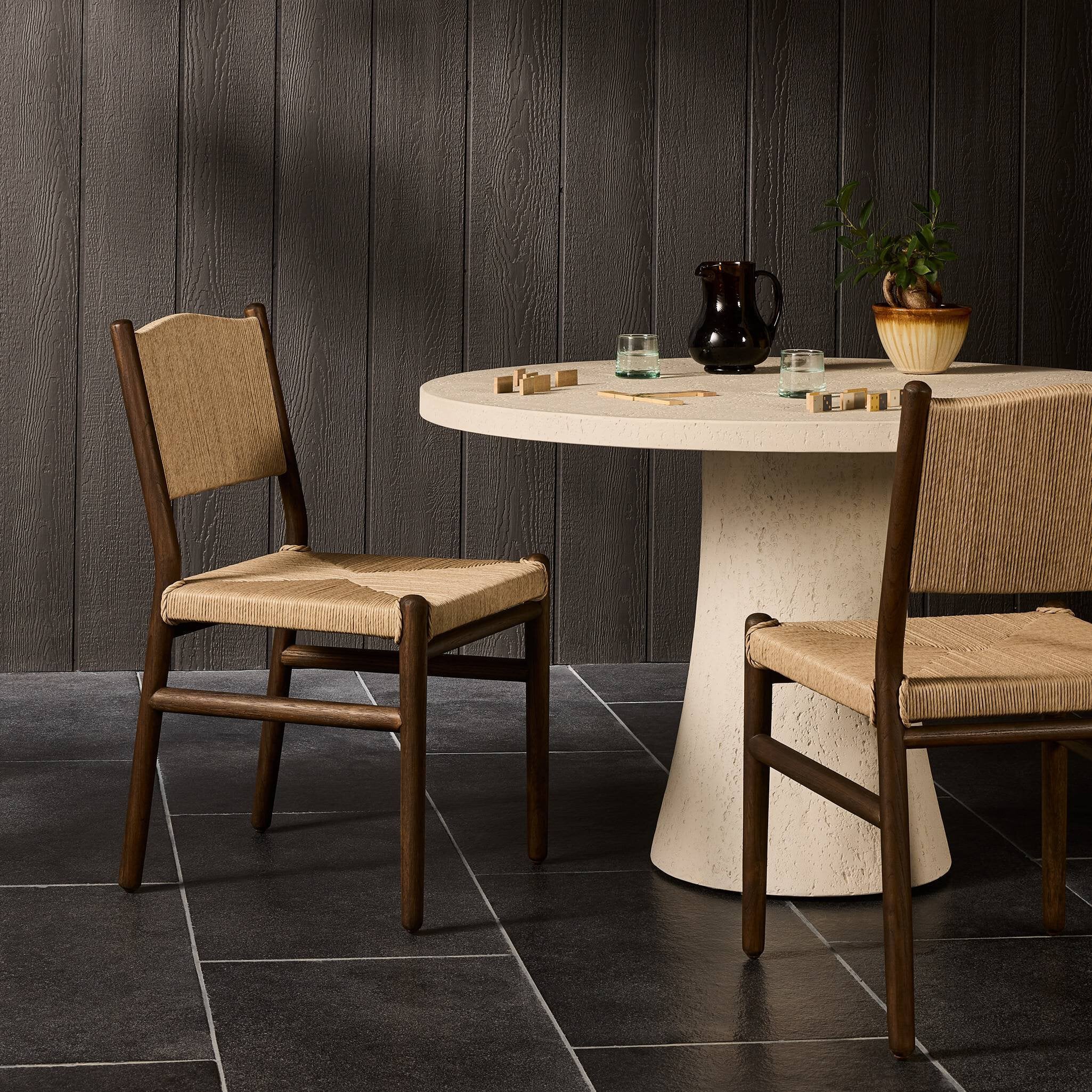 Round dining table with two wooden chairs against a dark paneled wall.