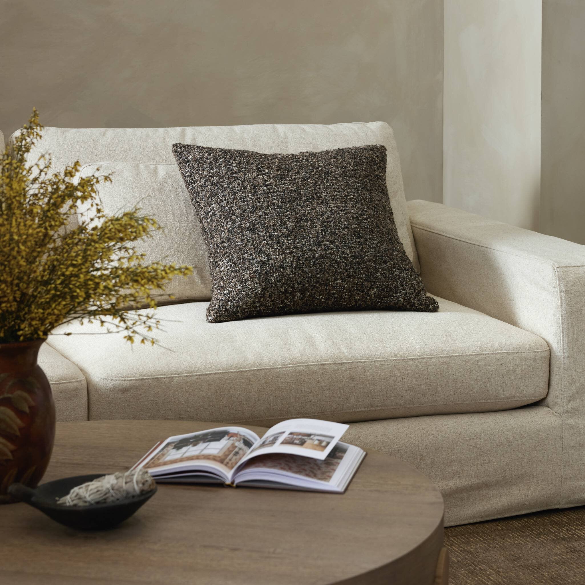 Beige sofa with a textured pillow, an open book, and a vase on a wooden coffee table.