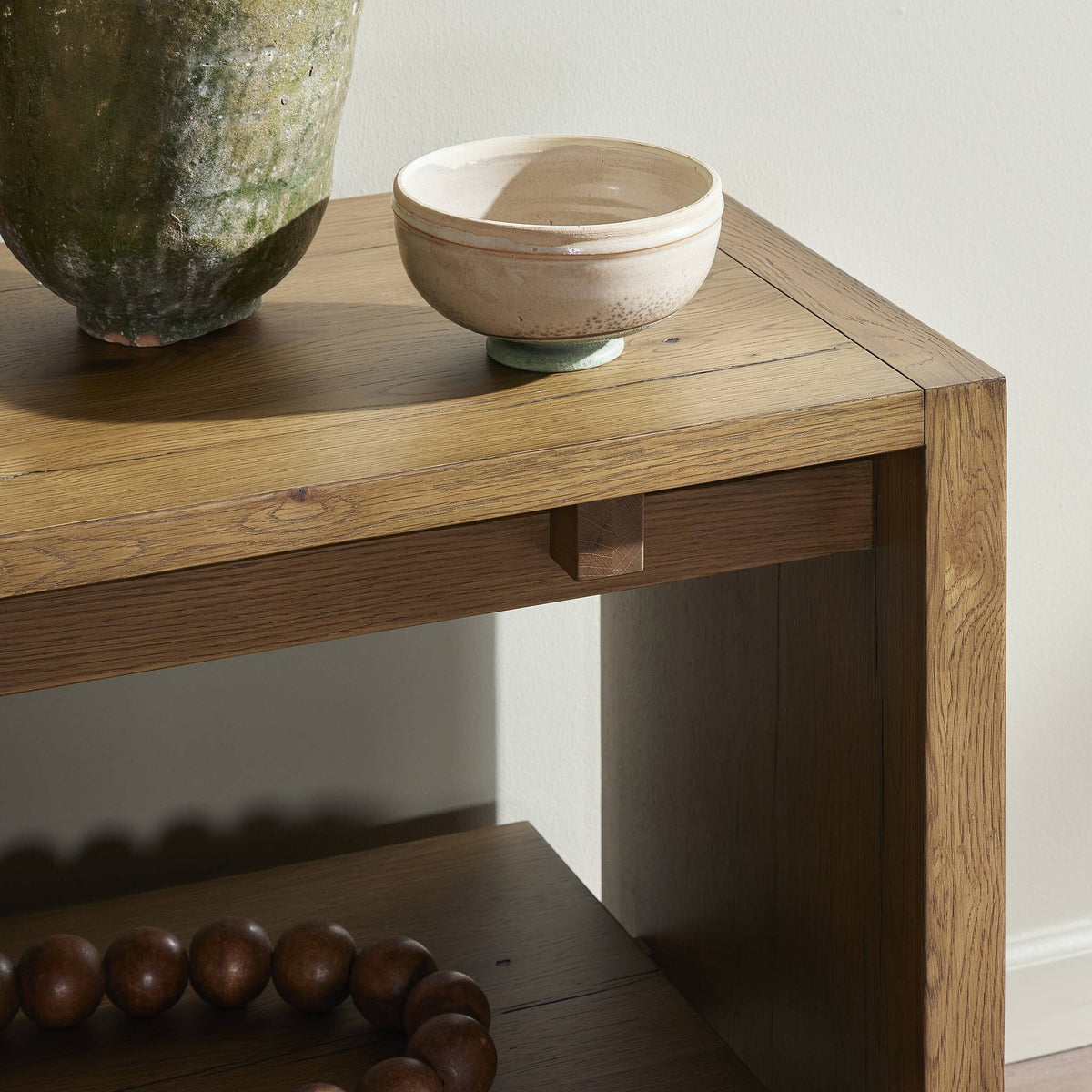 Wooden console table with a ceramic bowl and vase against a neutral wall.