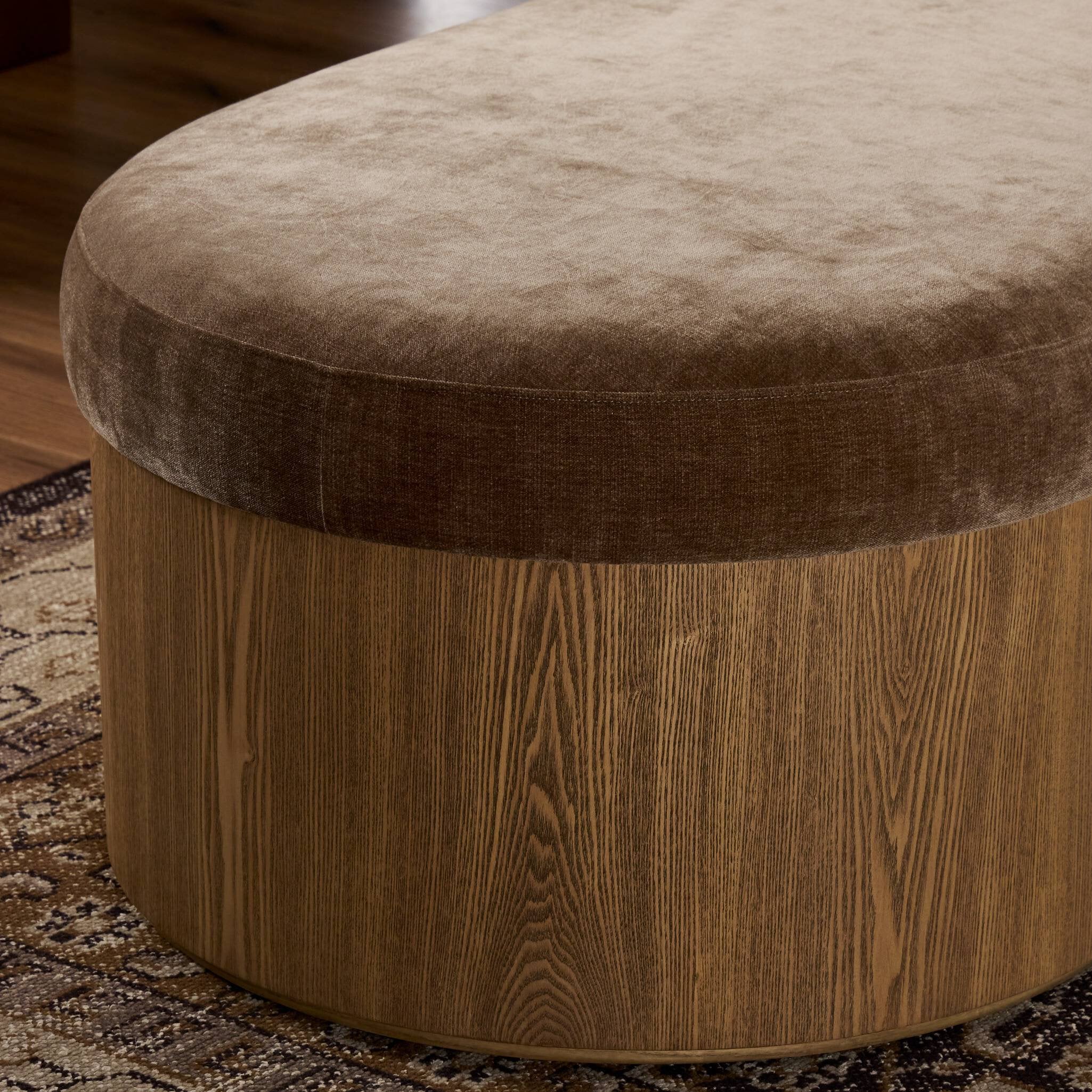 Round ottoman with brown cushion top and wooden base on a patterned rug